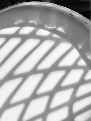 Shadows of a fence or railing cast onto a rounded surface, creating a pattern of lines in black and white.
