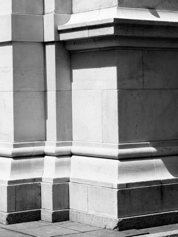 Close-up of a stone building corner with decorative molding and shadows.