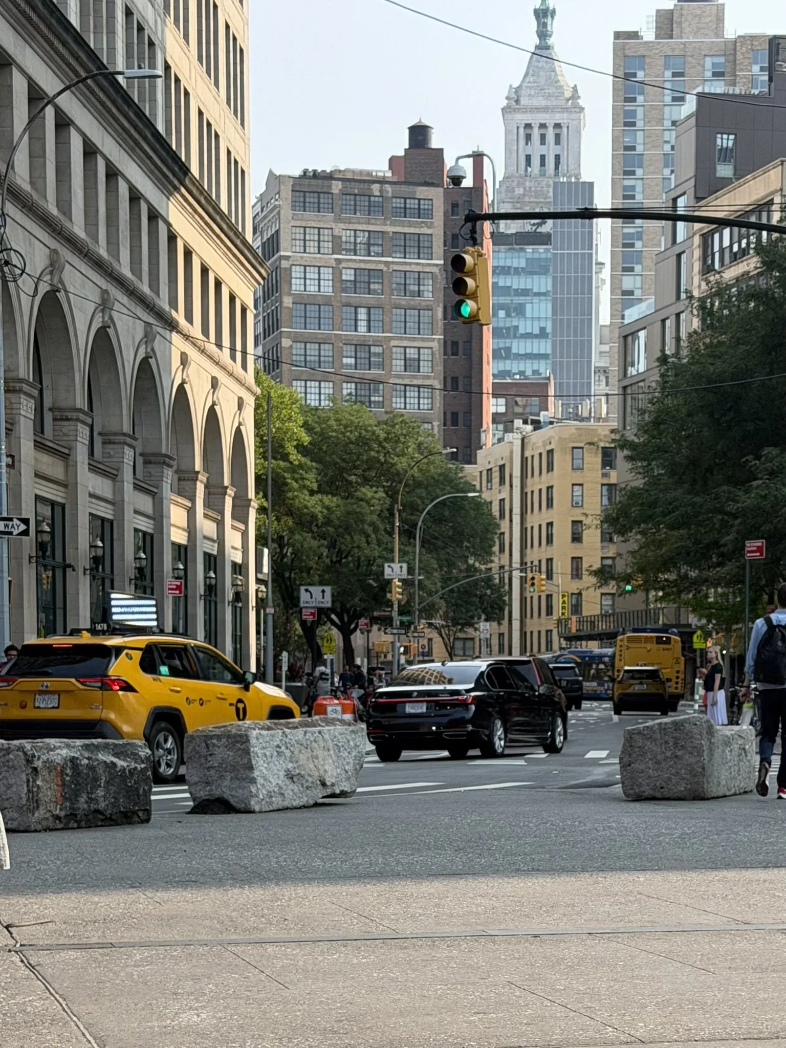 City street scene with yellow taxi, black cars, and city buildings including a prominent clock tower in the background.