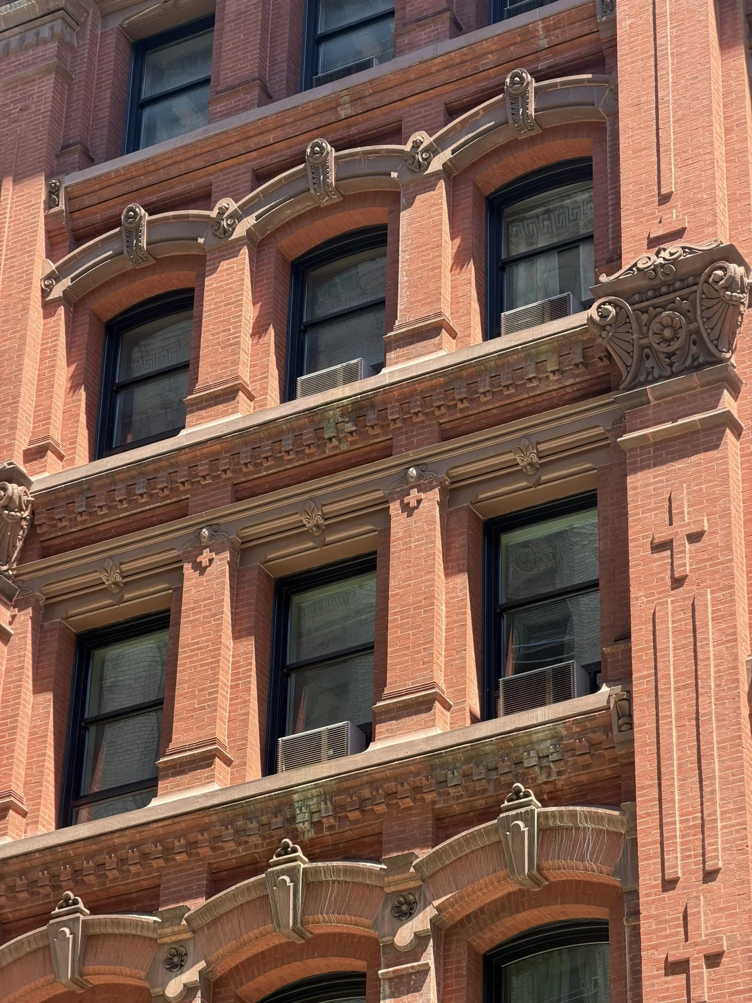 Close-up of a red brick building facade with ornate architectural details, including decorative corbels, window trims, and intricate stonework around the windows.