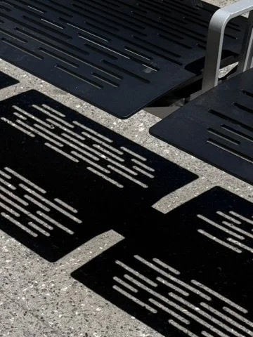 Black metal slats with engraved text resting on a concrete surface, likely plaques or decorative panels.