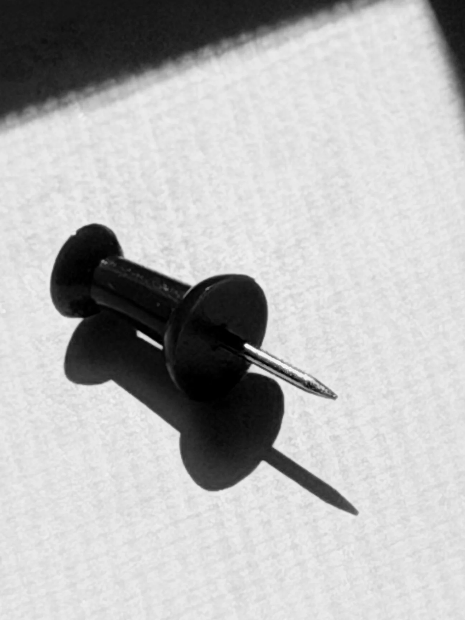 A black pushpin placed on a white surface, casting a shadow.