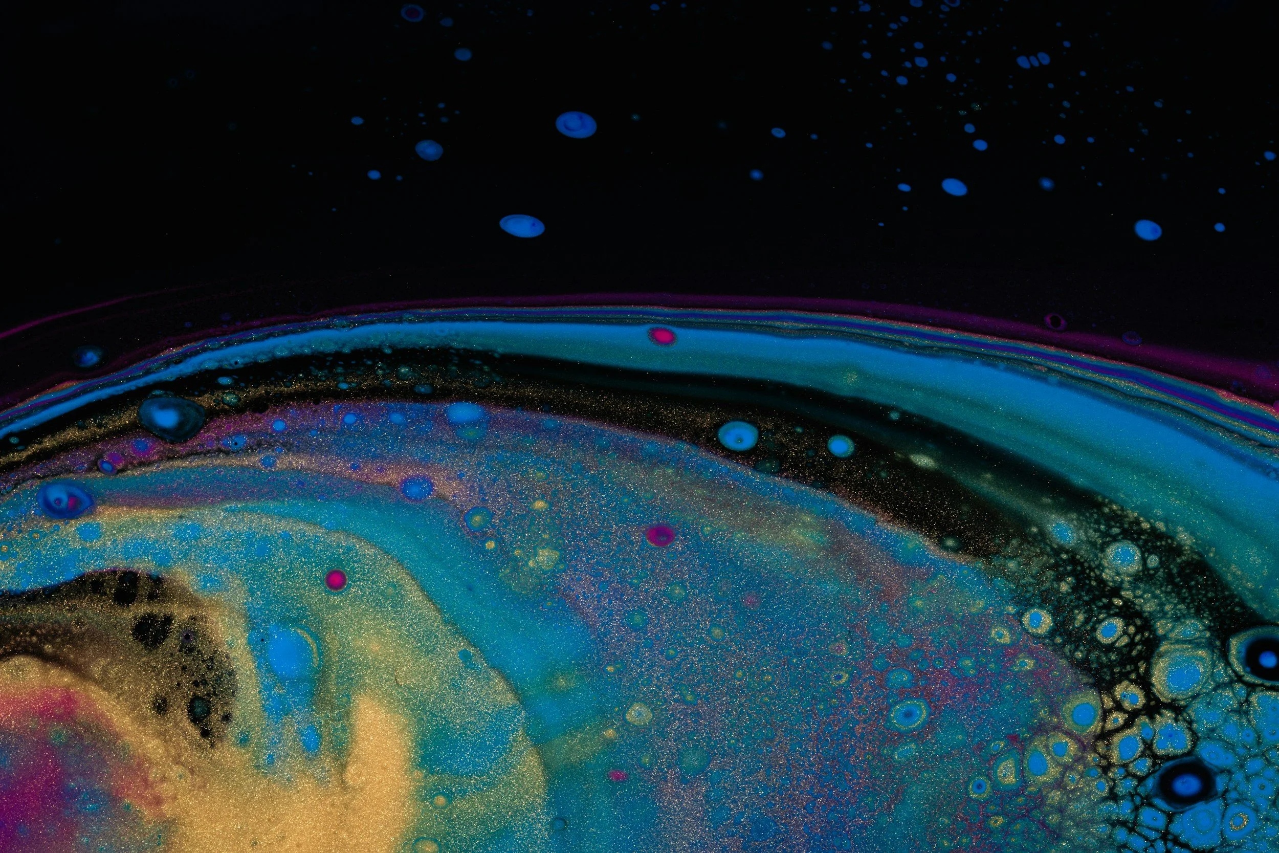 Abstract colorful liquid or paint swirling with blue, pink, gold, and black hues.