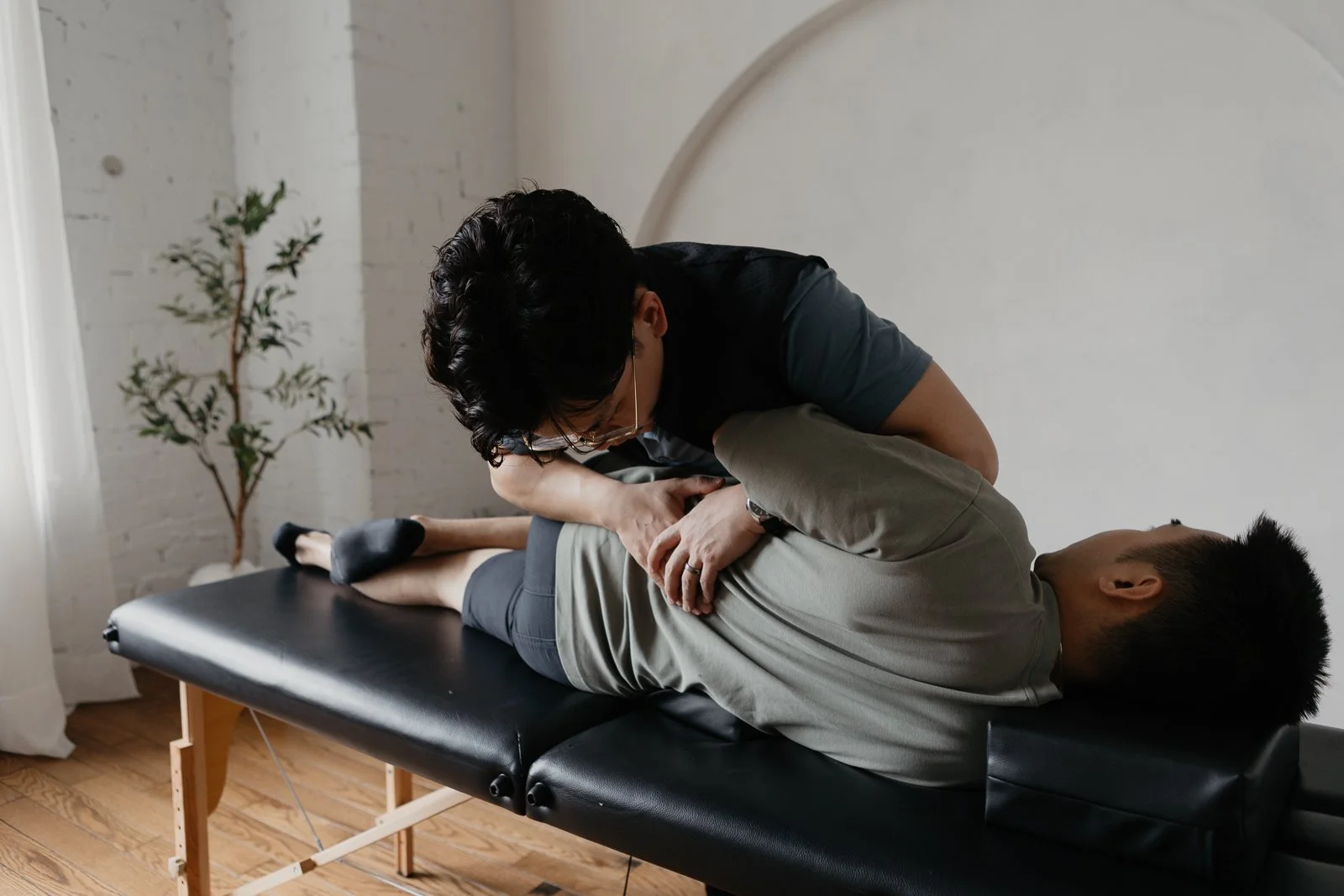 A person lying on a black therapy table receiving chiropractic or physical therapy treatment from a practitioner.