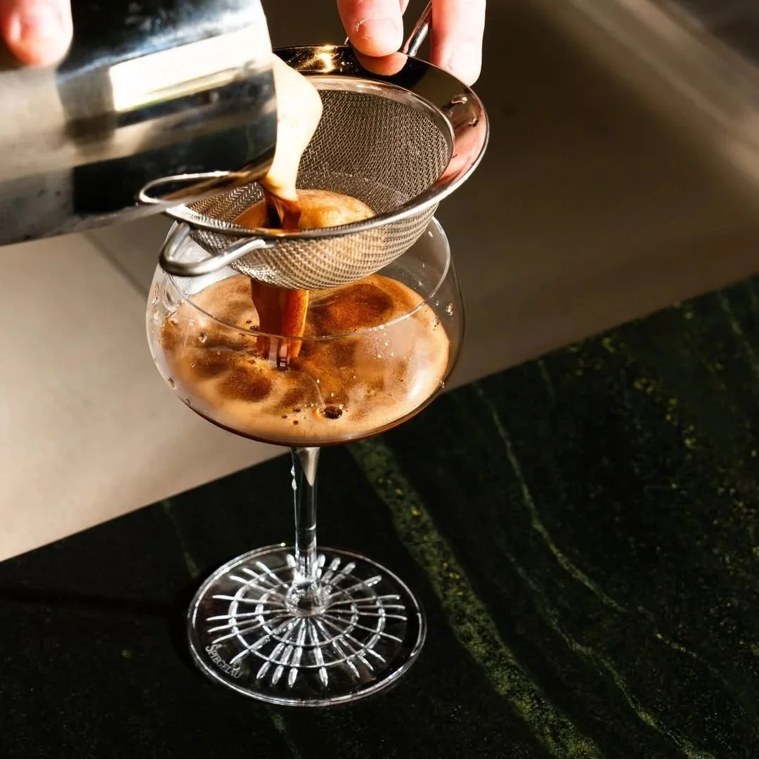 Coffee being poured into a cocktail glass through a fine mesh strainer.