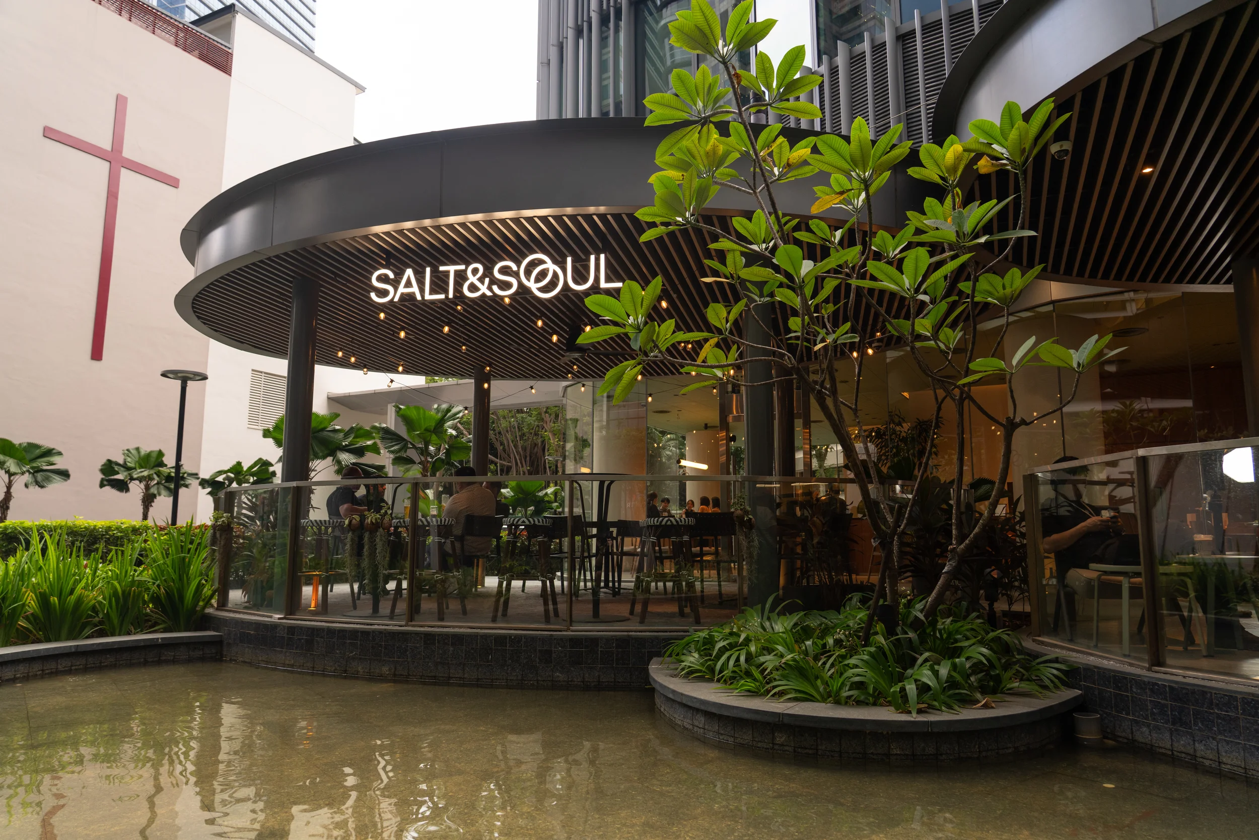 Exterior view of a restaurant named Salt & Soul with outdoor seating, greenery, and modern architecture in an urban area.