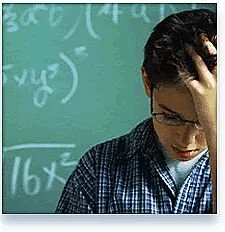 A person with glasses and dark hair looking down, touching their head, in front of a chalkboard with mathematical equations.