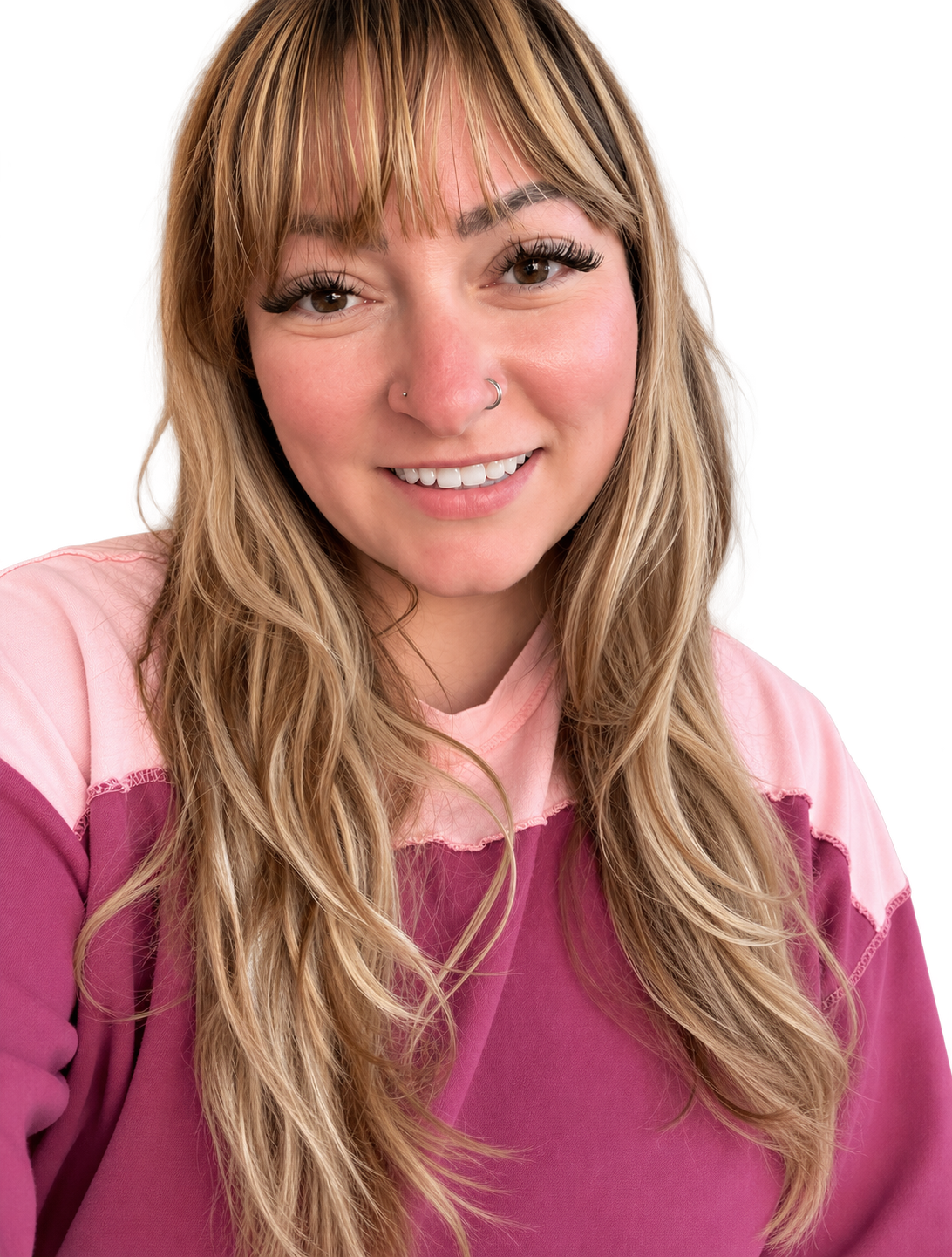 Smiling young woman with long wavy blonde hair, bangs, nose piercings, and a pink sweatshirt