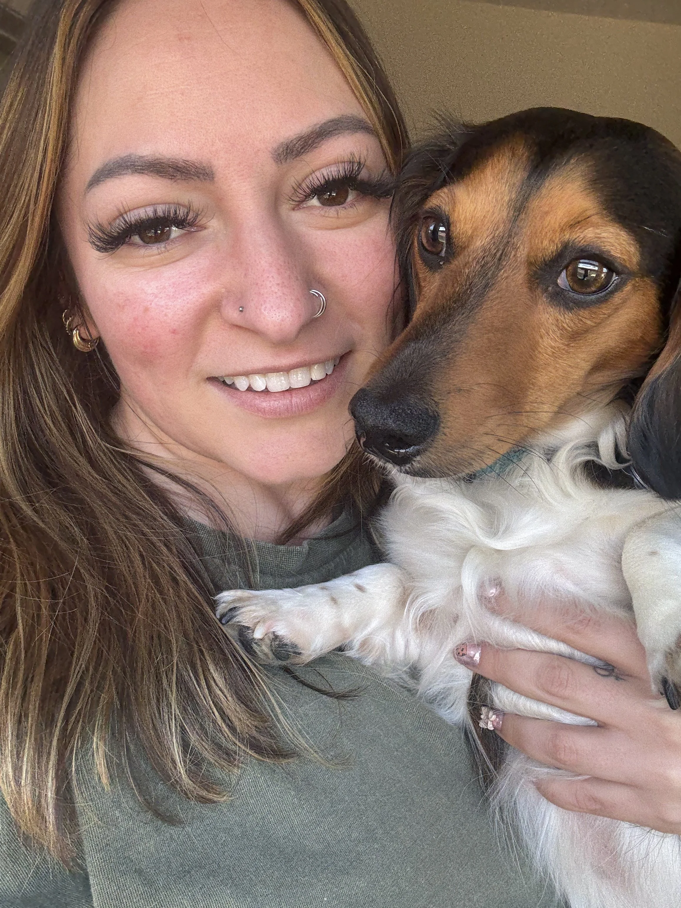 Smiling woman cuddling two dogs, including a German Shepherd and a small white dog.