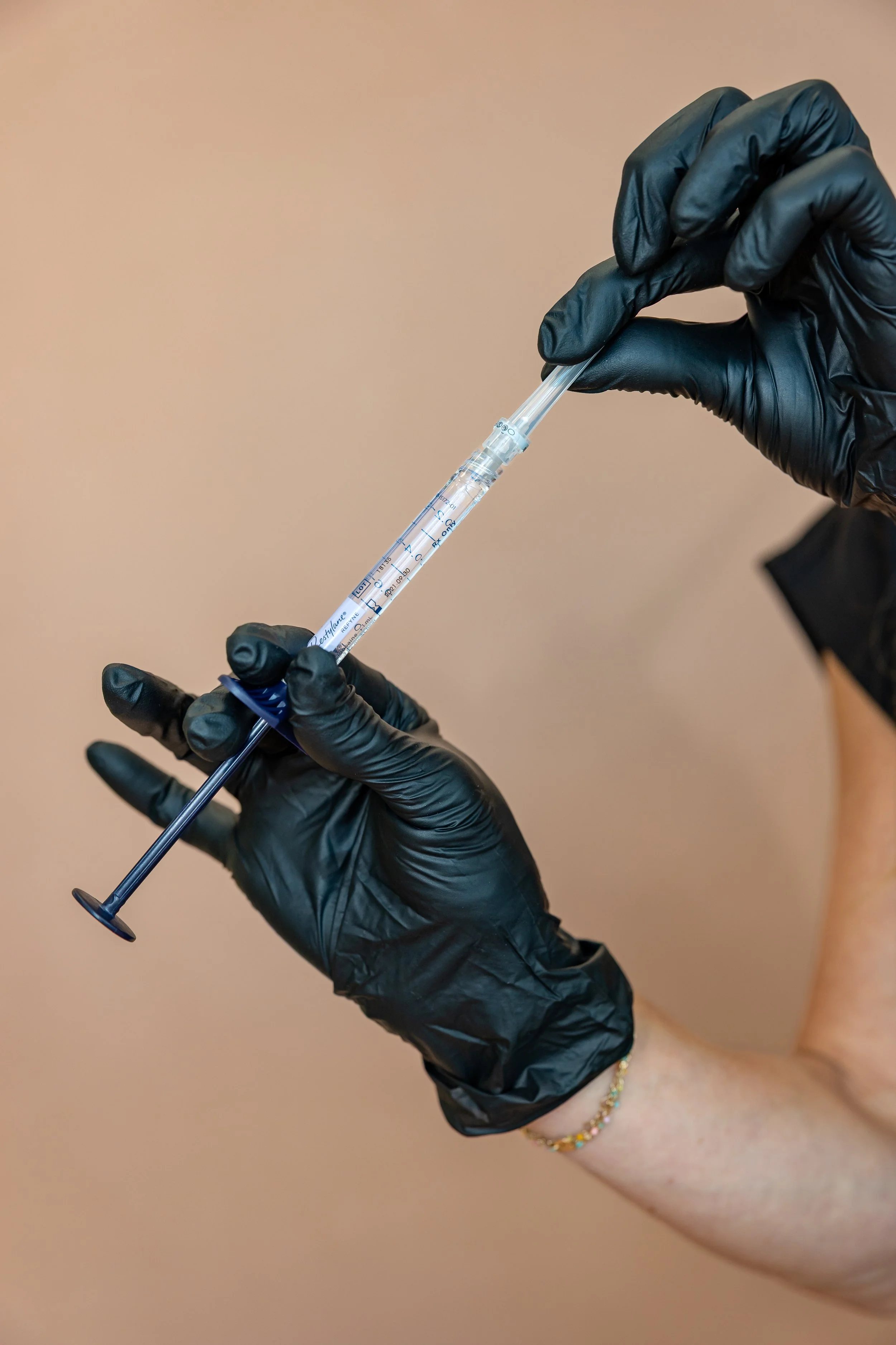 A person wearing black gloves holding a syringe with a needle, preparing for an injection.