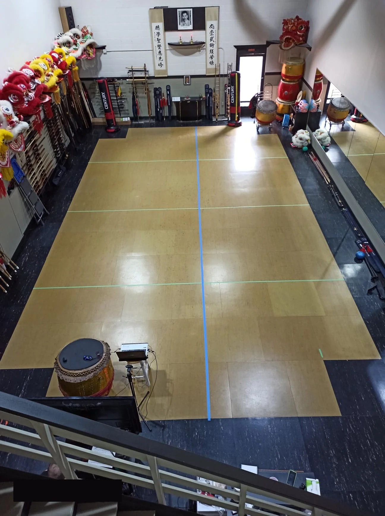 Empty martial arts training room with a wooden floor, surrounded by lion dance costumes, drums, and traditional Chinese decorations.