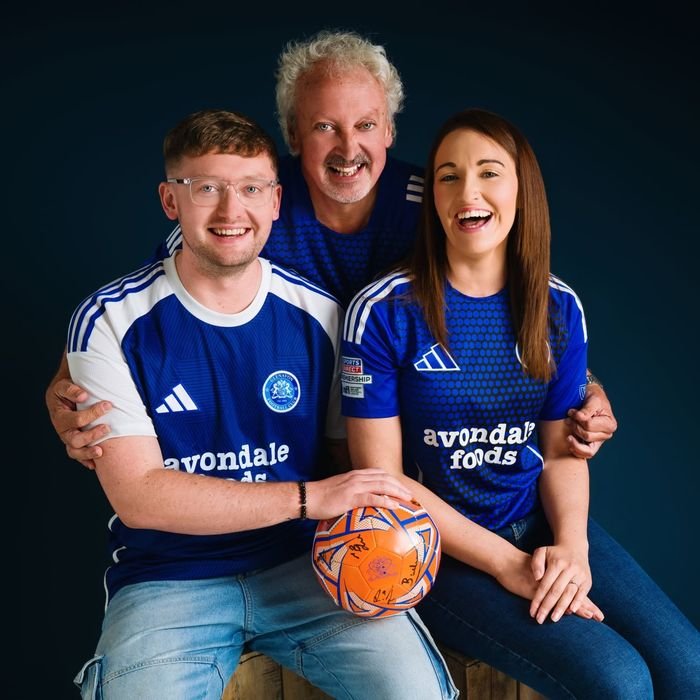 Three supporters in club shirts with a signed ball