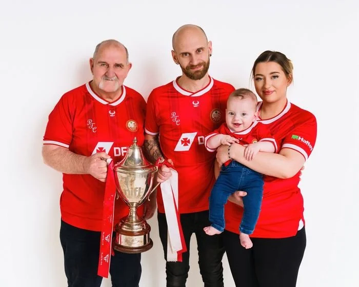 Three generations in football shirts with the league trophy