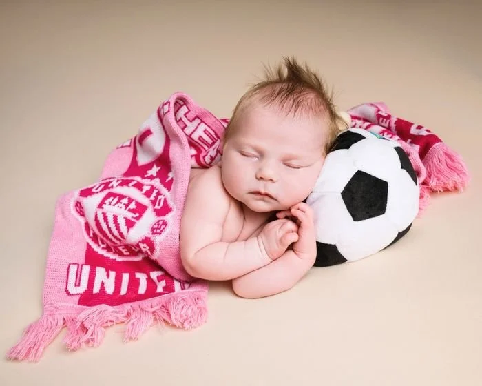 Newborn asleep with a football scarf and ball