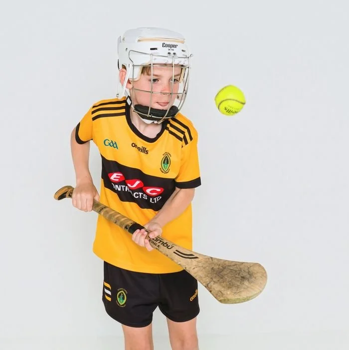 Boy in a hurling helmet striking a sliotar