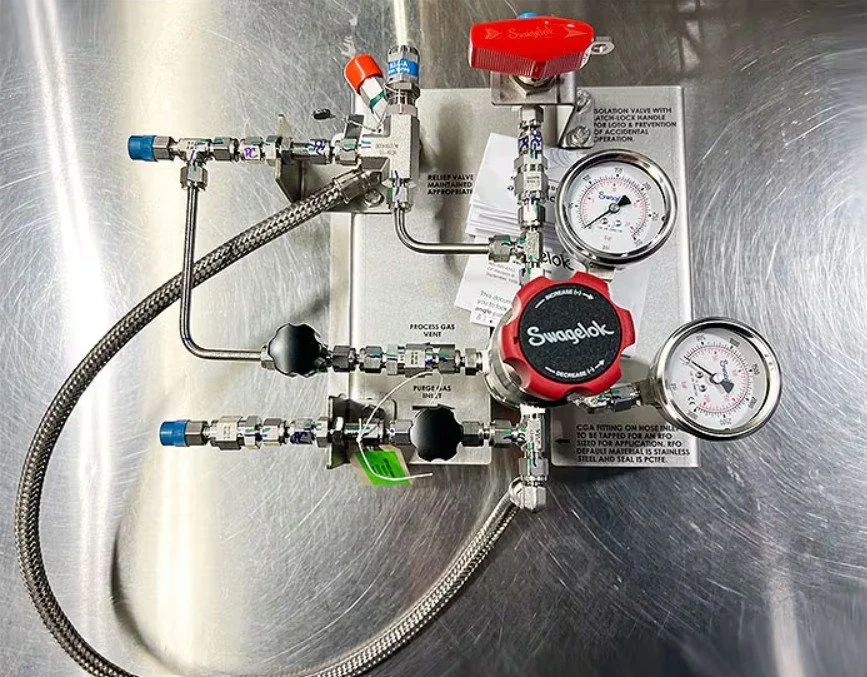 A stainless steel industrial gas control panel with gauges, valves, and tubing for regulating gas flow.