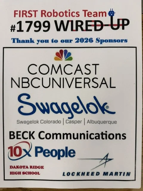 Sign displaying acknowledgment of sponsors for FIRST Robotics Team 1799 WIRED UP, including Comcast NBCUniversal, Swagelok Colorado, Casper, Albuquerque, BECK Communications, 10X People, Dakota Ridge High School, and Lockheed Martin.