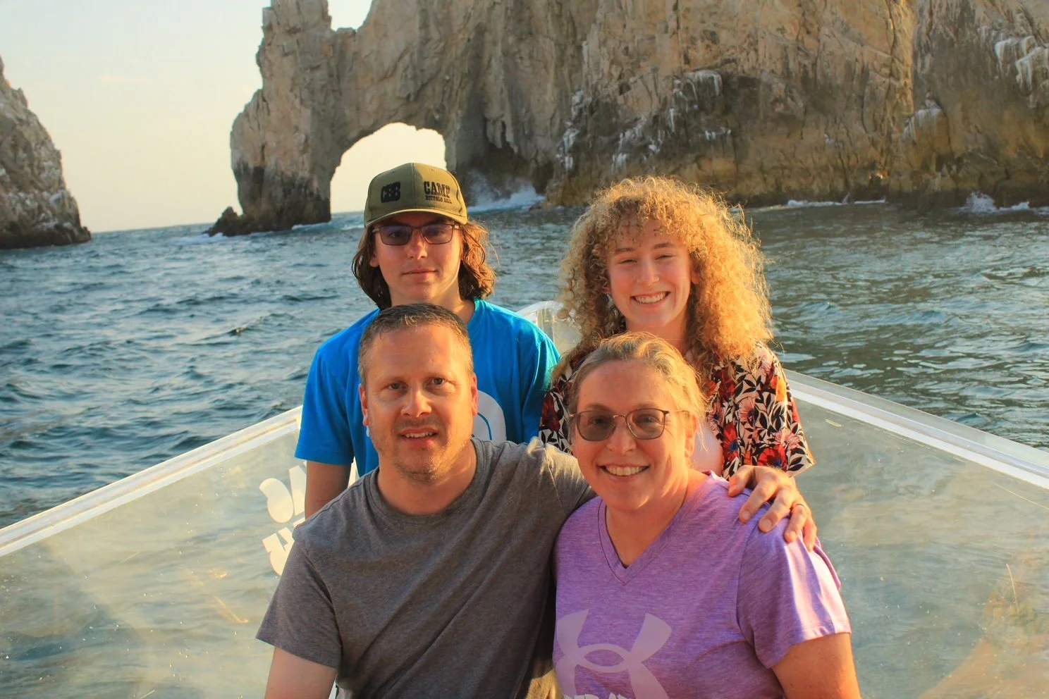 Andy and his family on a boat with rocky coastal cliffs in the background, during sunset, smiling at the camera.