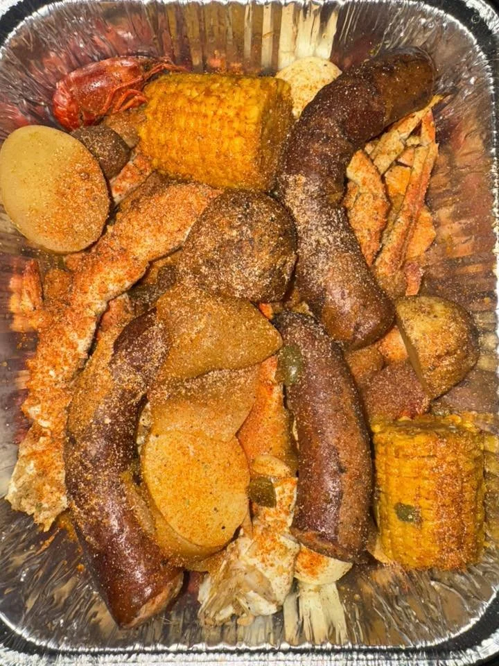 Cooked seafood boil with shrimp, crab, potatoes, sausage, and corn in a foil tray.