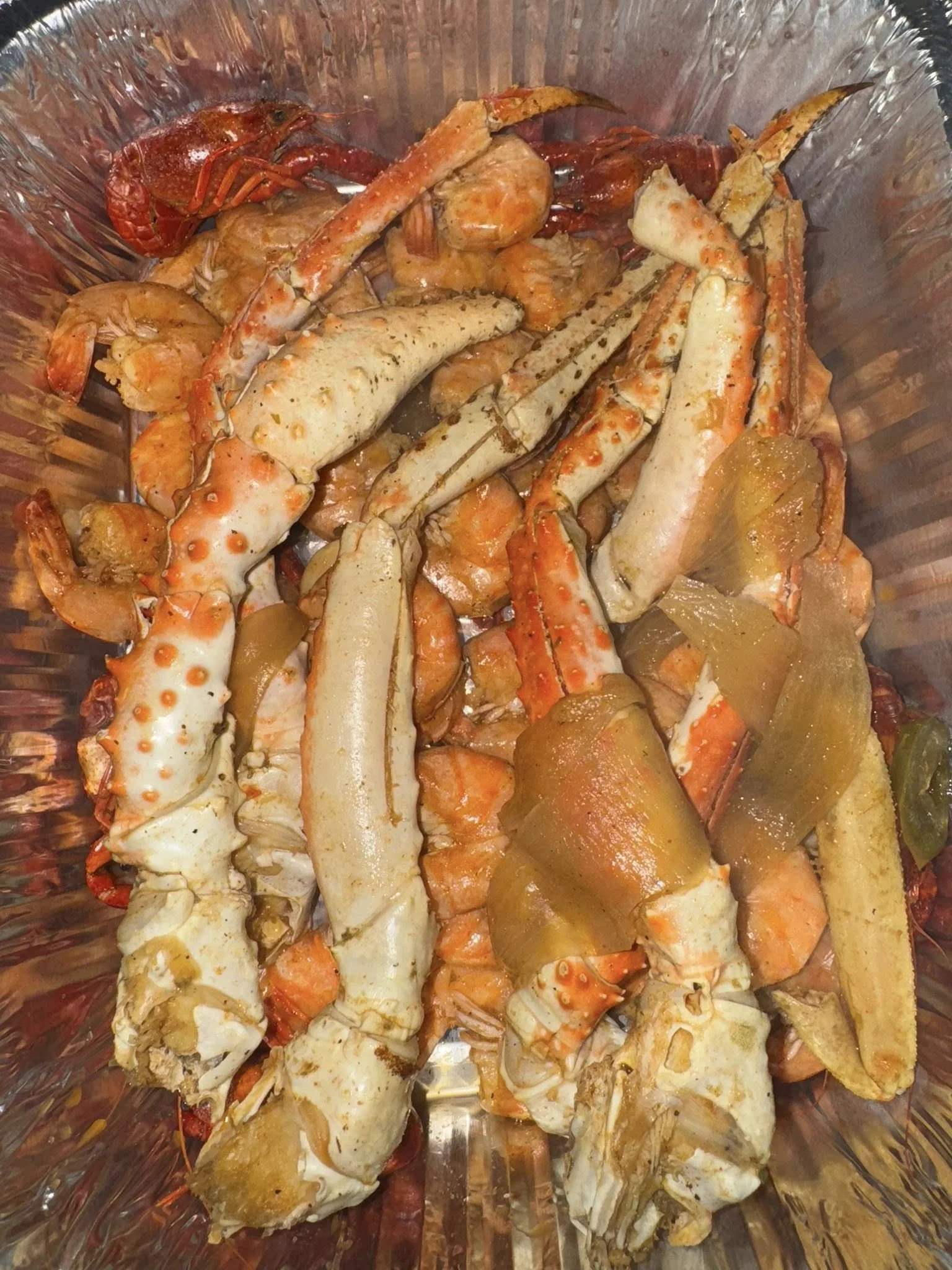 Various cooked seafood including lobster, crab legs, shrimp, and possibly scallops in a glass or metal container.