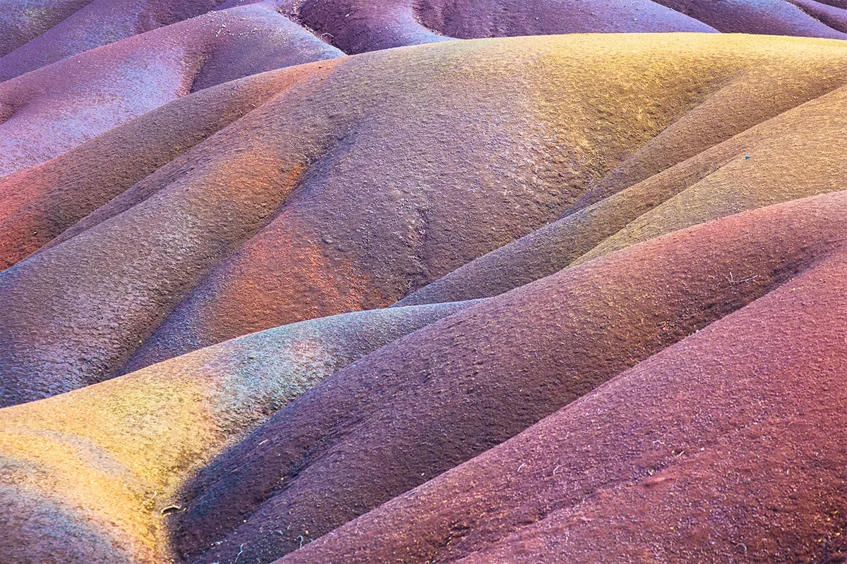 Close-up view of colorful, rolling sand dunes with smooth, rippled textures in purple, yellow, and orange hues.
