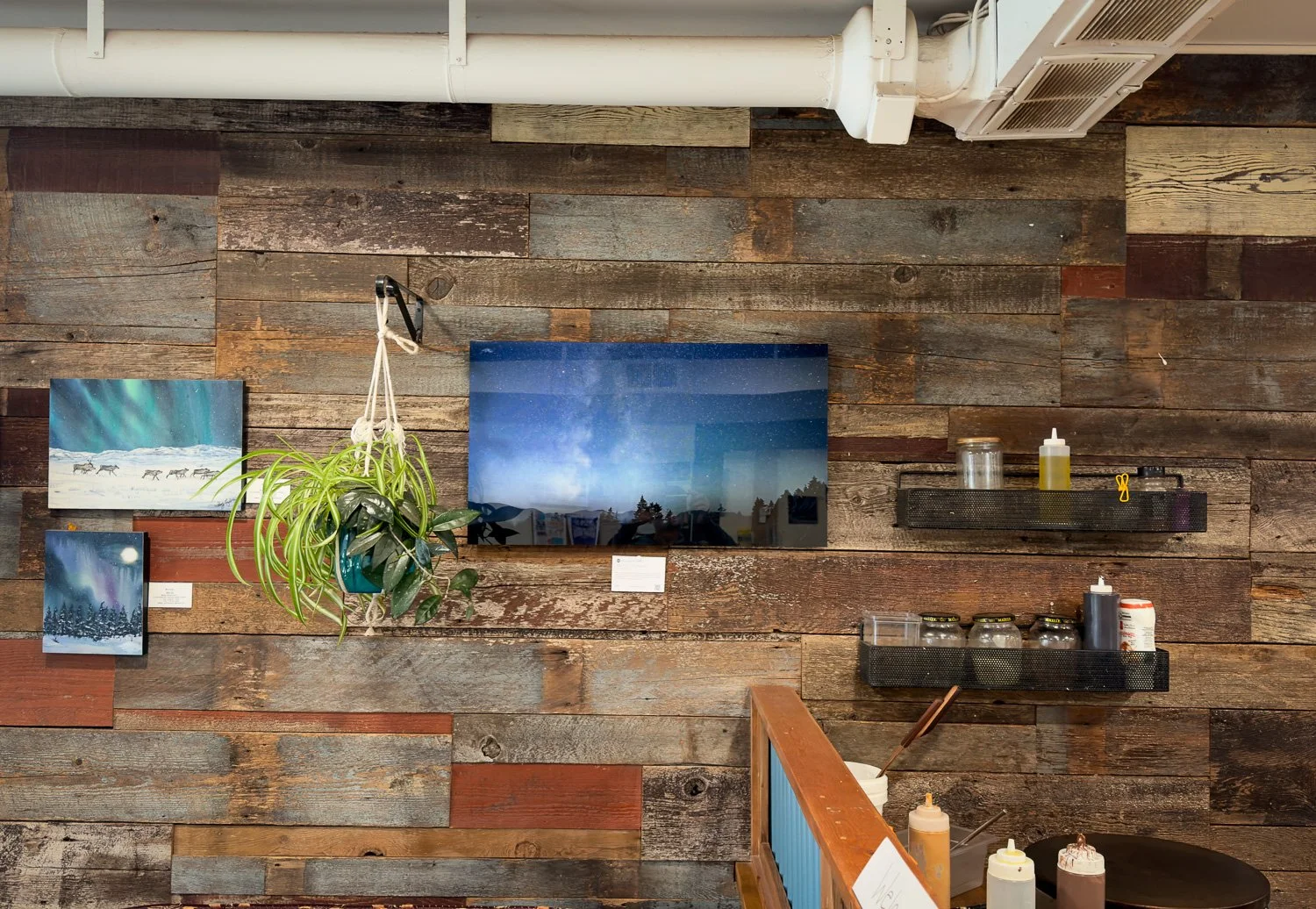 Large acrylic print of the Milky Way over a silhouetted forest, displayed on a reclaimed-wood wall at Bombers Brewing in Port Alberni.