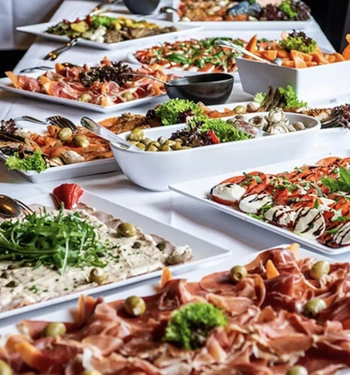 Assorted dishes of salads and appetizers arranged on a table, including cold cuts, vegetables, and garnished plates.