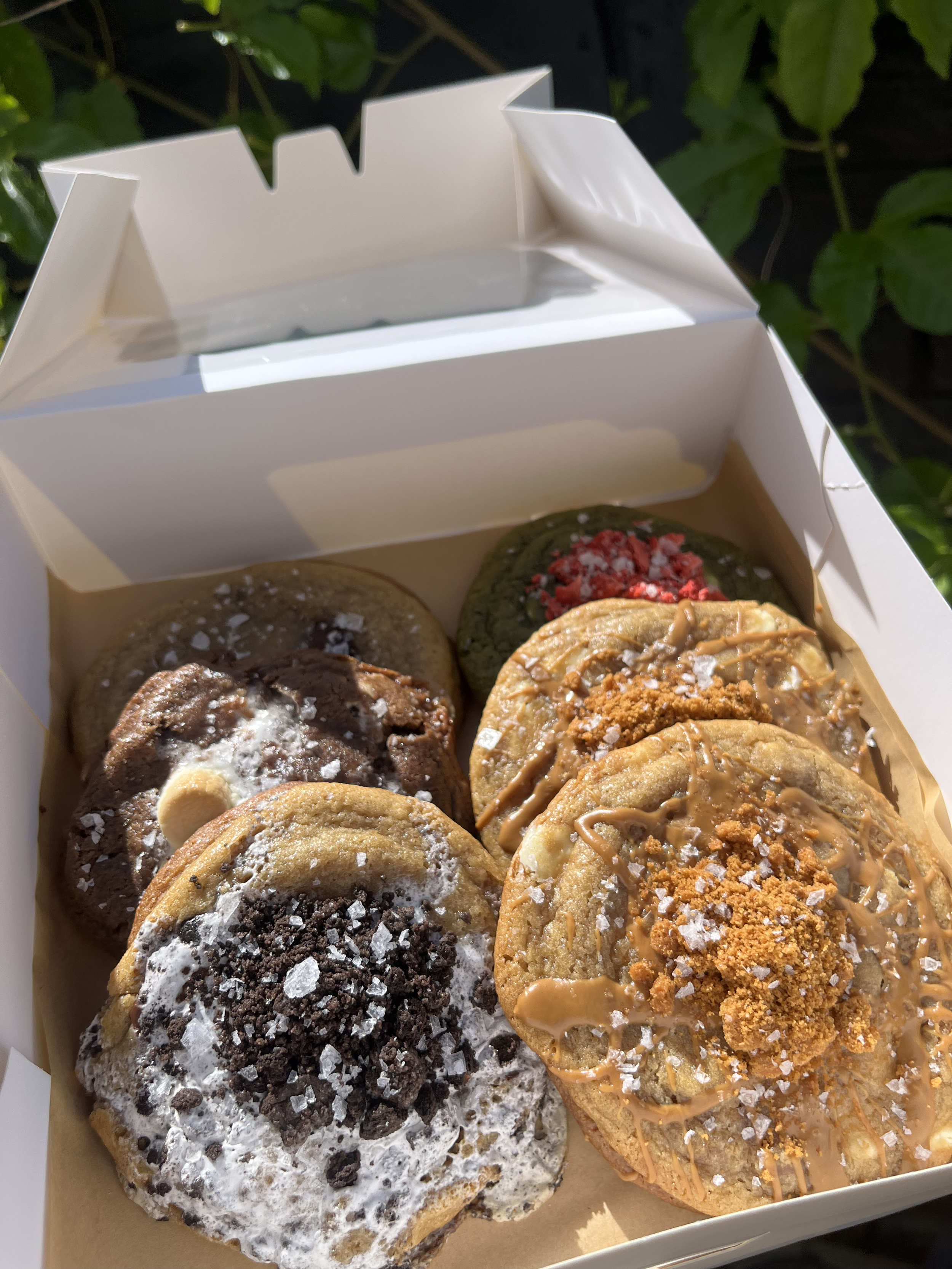 A box of assorted donuts with various toppings and flavors, some with chocolate, caramel, and sprinkles, on a brown paper lining.