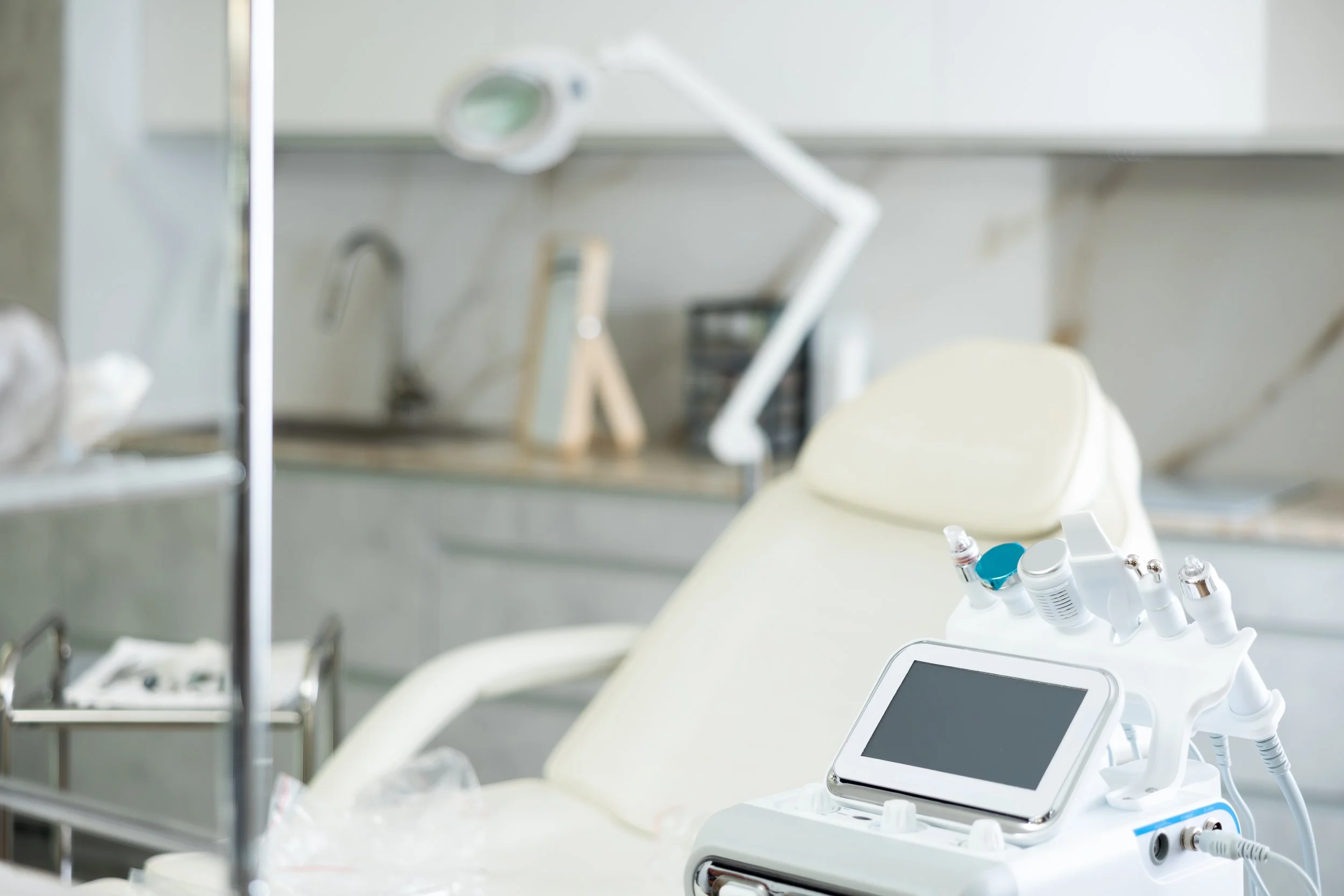 Medical examination room with dental or surgical equipment, including a portable device with multiple attachments and a tablet, in front of a dental chair.