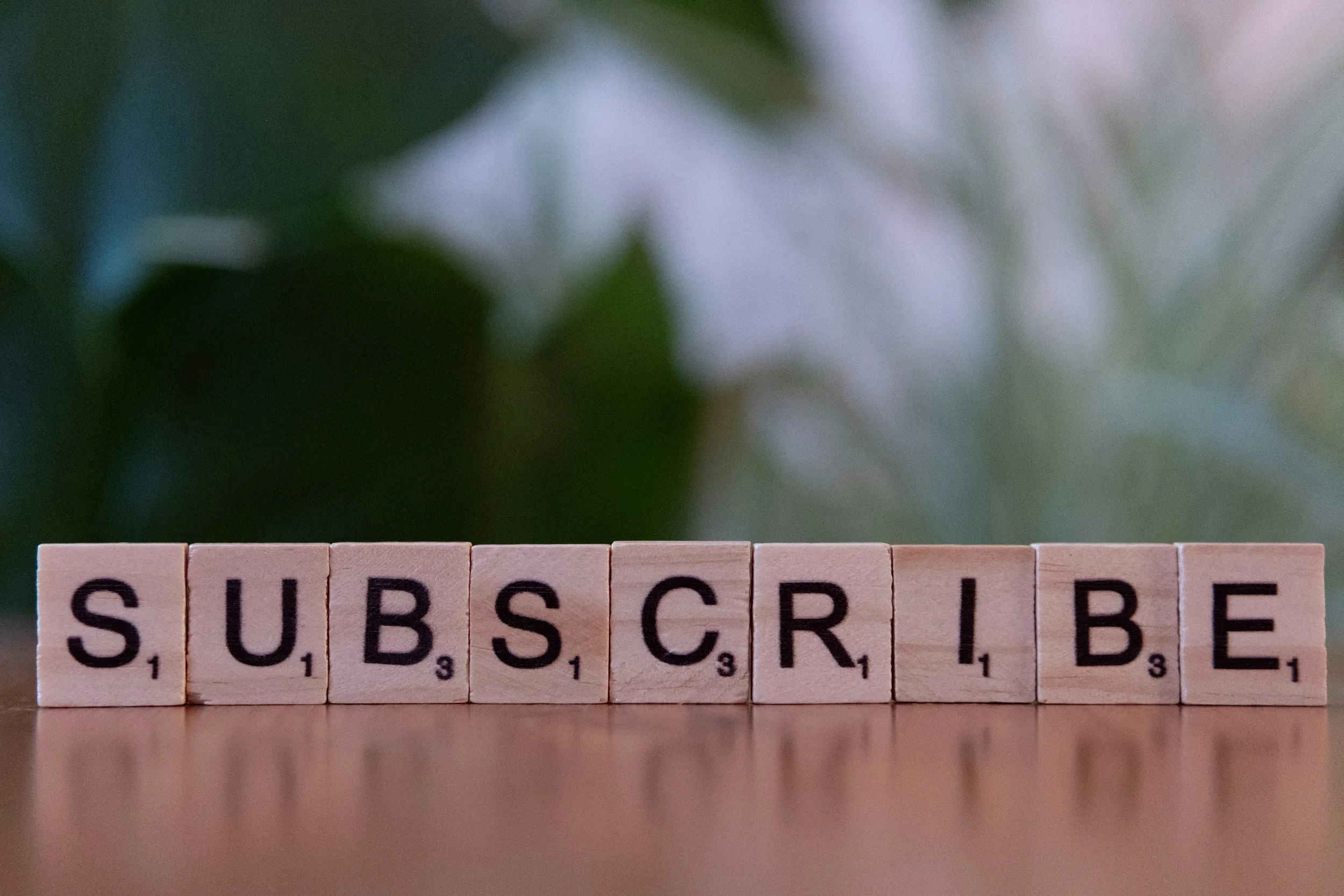 Wooden tiles spelling out 'SUBSCRIBE' in black letters on a wooden surface with a blurred background.