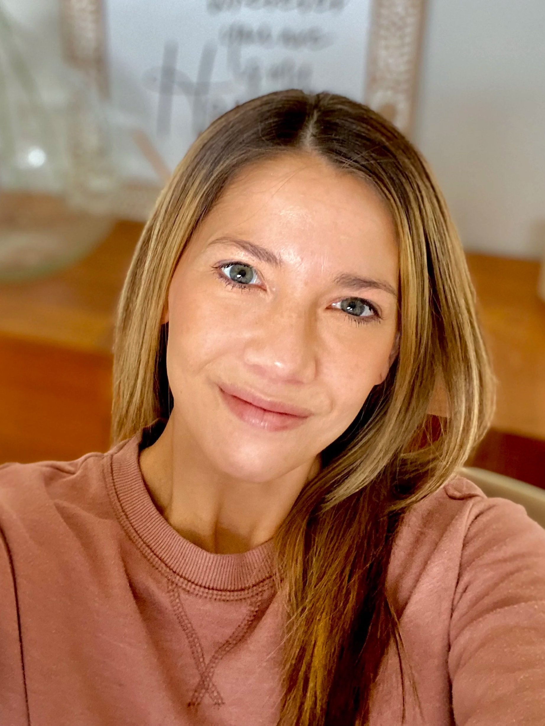 Close-up of a smiling woman with light brown hair and blue eyes wearing a pinkish sweater.