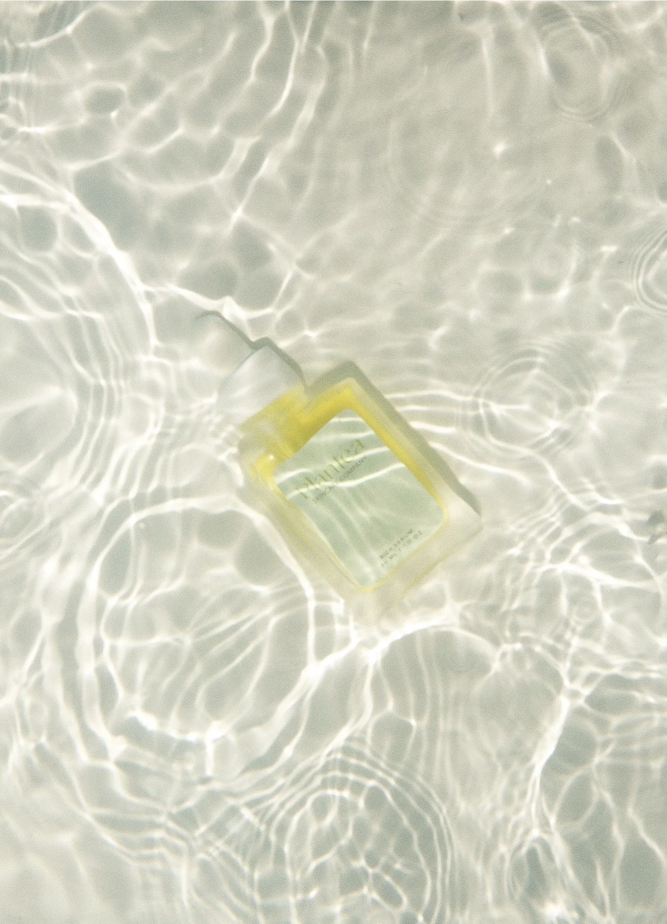 A plastic bottle floating in light-reflecting water creating rippling patterns.