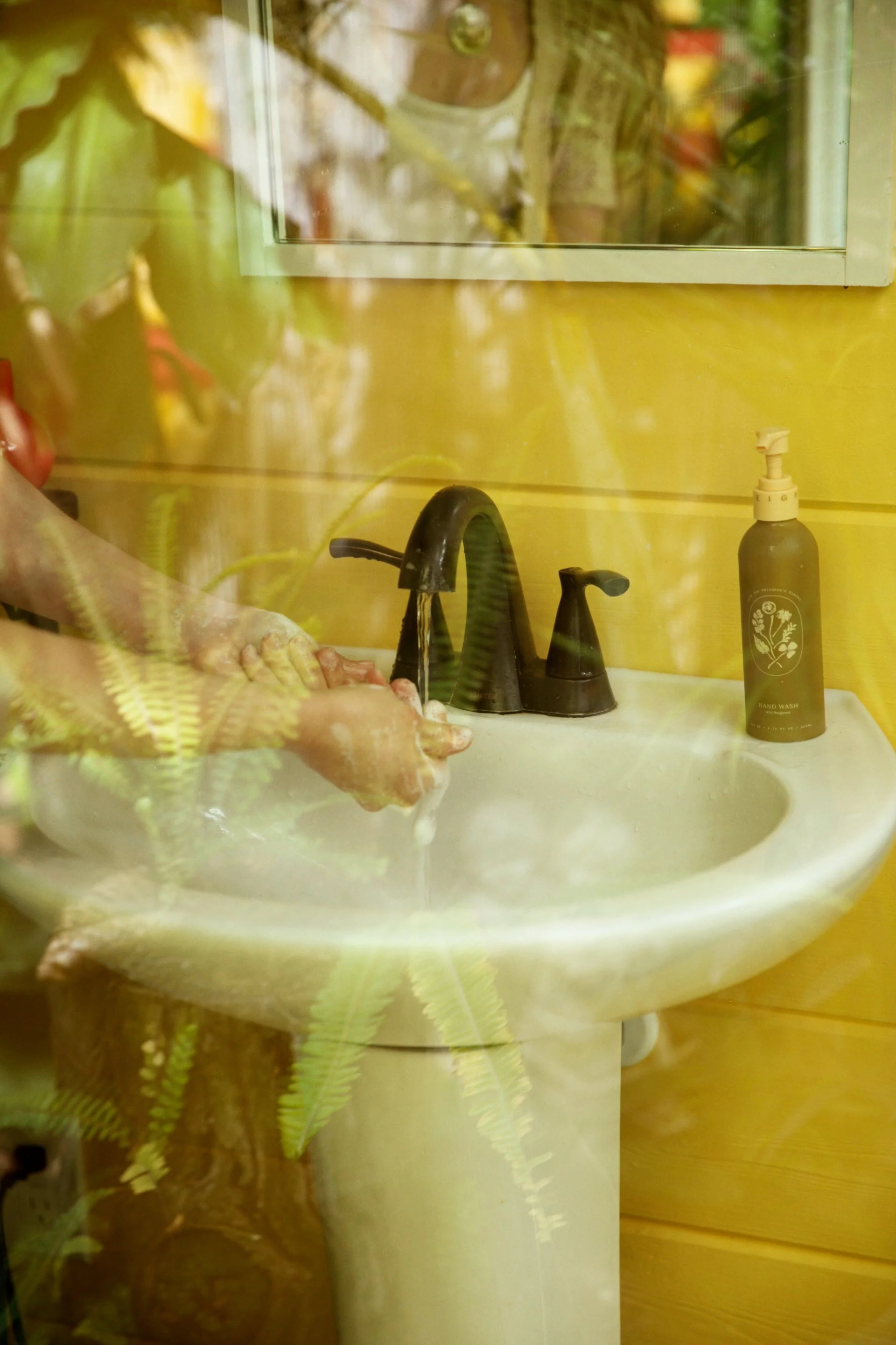 A bathroom sink with a black faucet, a soap dispenser labeled 'hand wash,' and a mirror above the sink. The mirror reflects part of the sink and the soap dispenser.