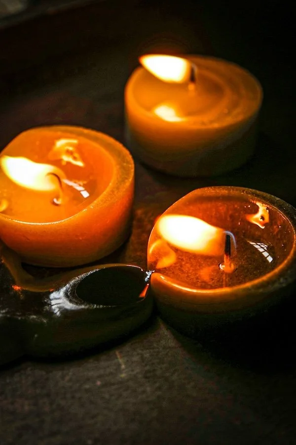 Four floating candles in small round containers on a dark surface, casting a warm glow.
