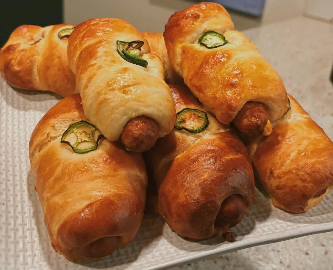 A plate of baked pigs in a blanket with jalapeño slices on top.