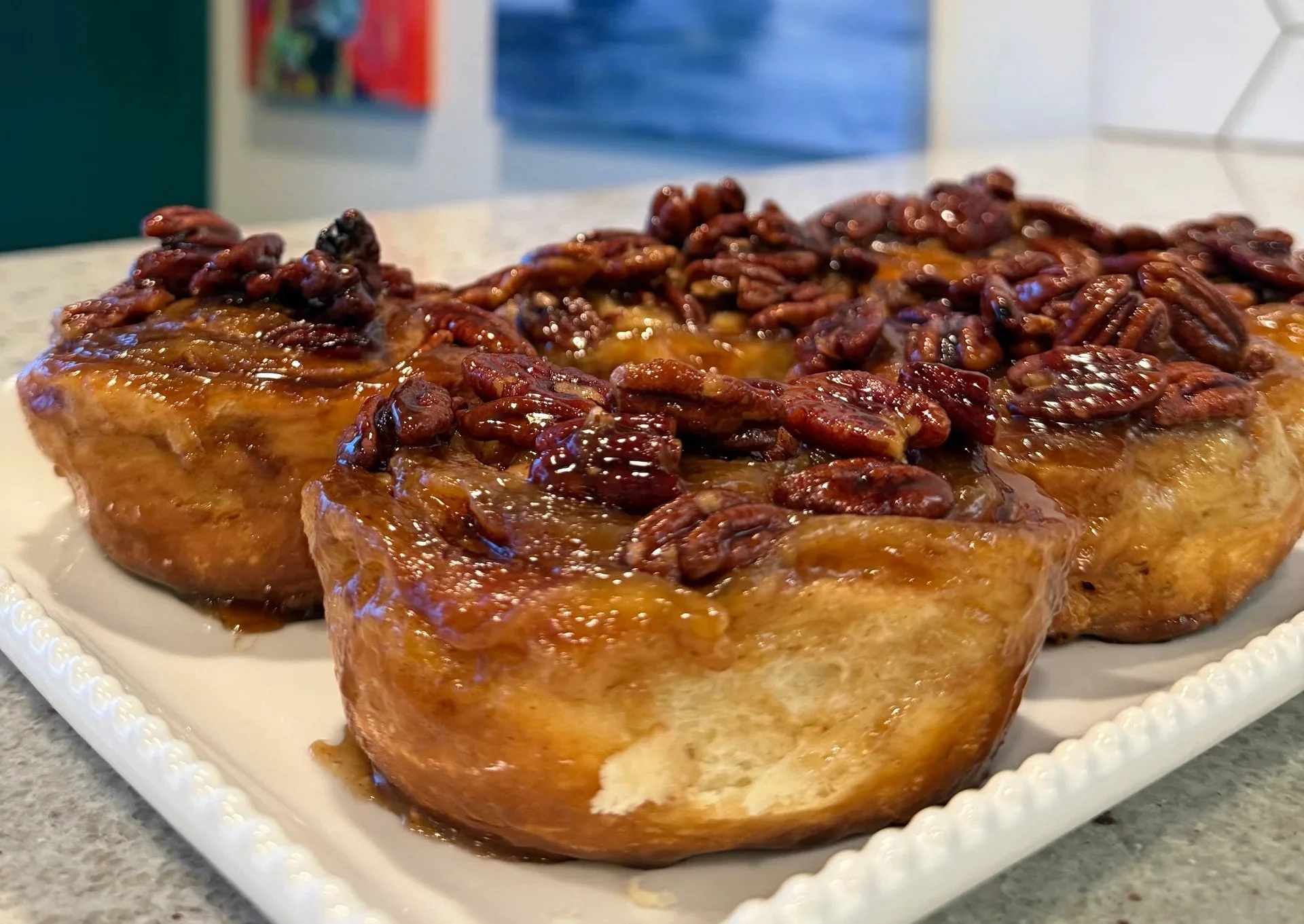 Two slices of caramel-glazed sweet potato topped with pecans on a decorative white plate.