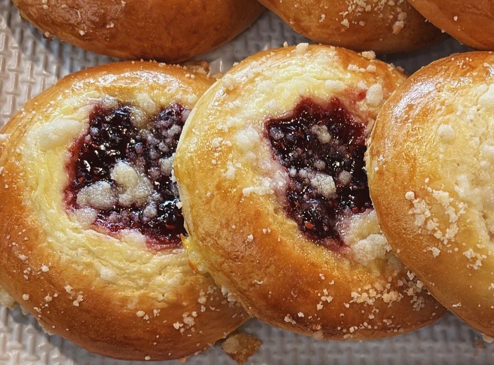 Close-up of two golden-brown baked buns filled with blueberry jam and sprinkled with sugar.