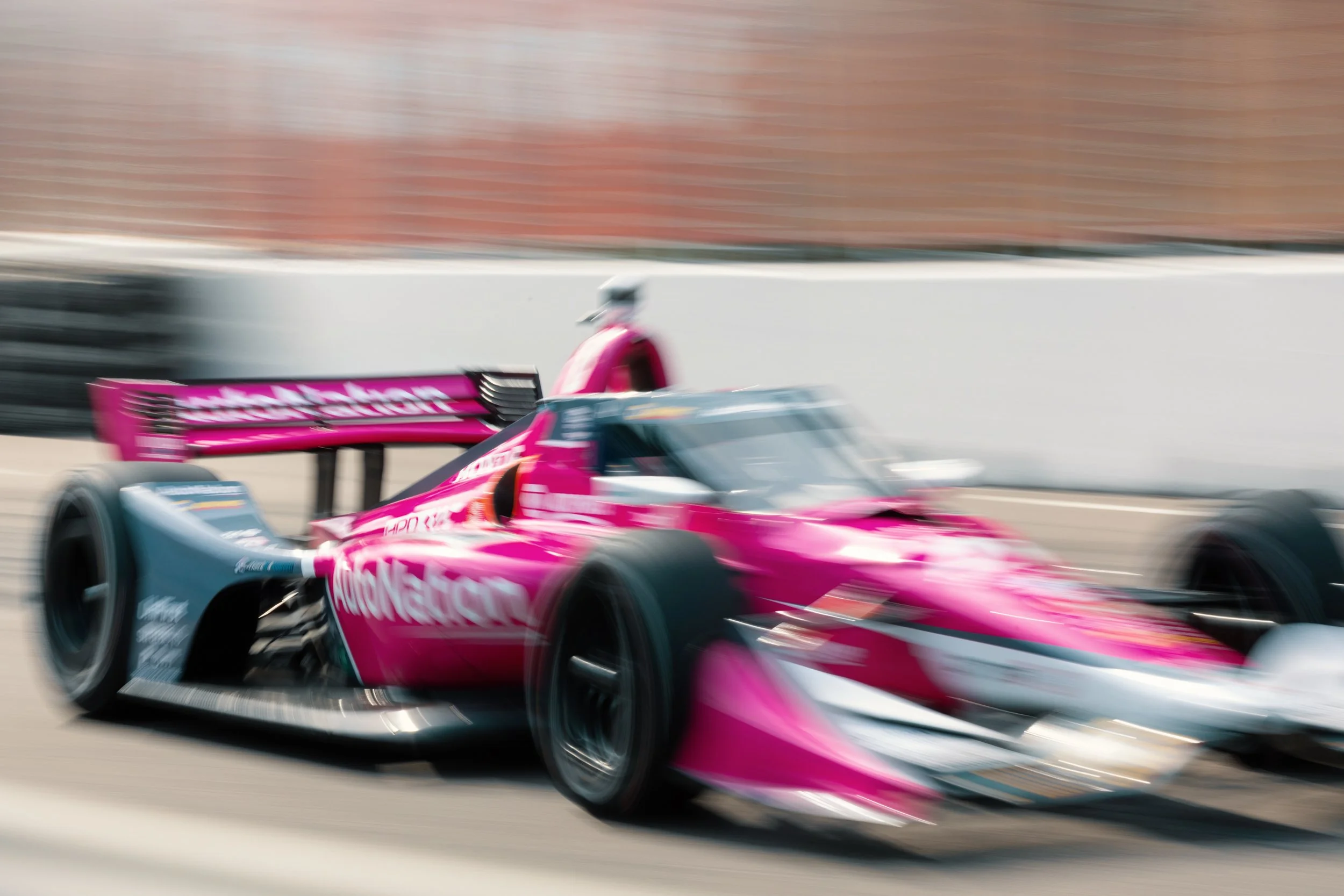 Cinematic motorsport photography of an IndyCar race car at high speed, captured with dramatic motion blur on a street circuit.