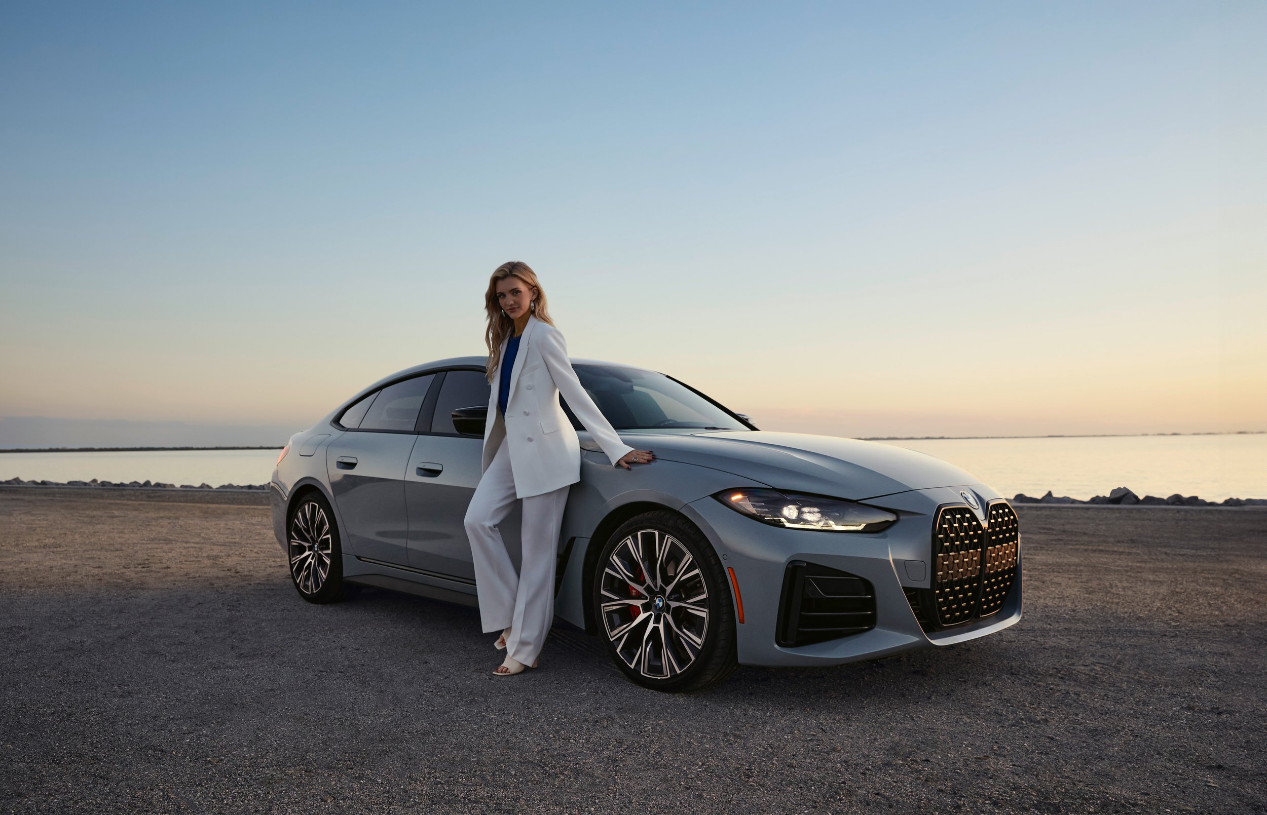 BMW automotive advertising-style photography featuring fashion talent with the M440i Gran Coupe at sunset