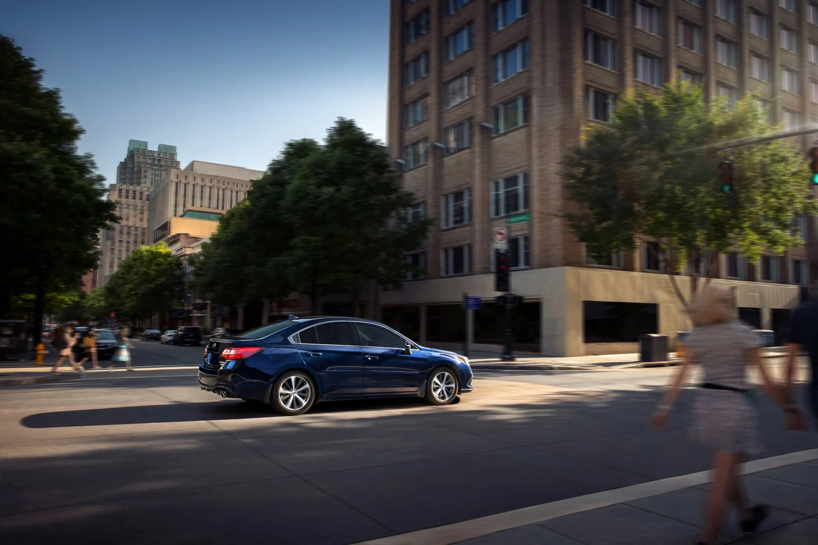 Commercial advertising photography of a Subaru Legacy sedan driving through a scenic city landscape during sunset.