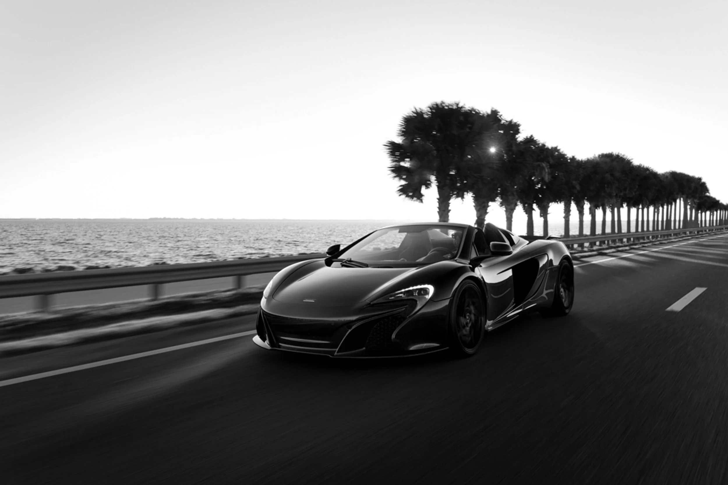 Dynamic commercial advertising photography of a luxury high-performance sports car speeding down a deserted highway at sunset.
