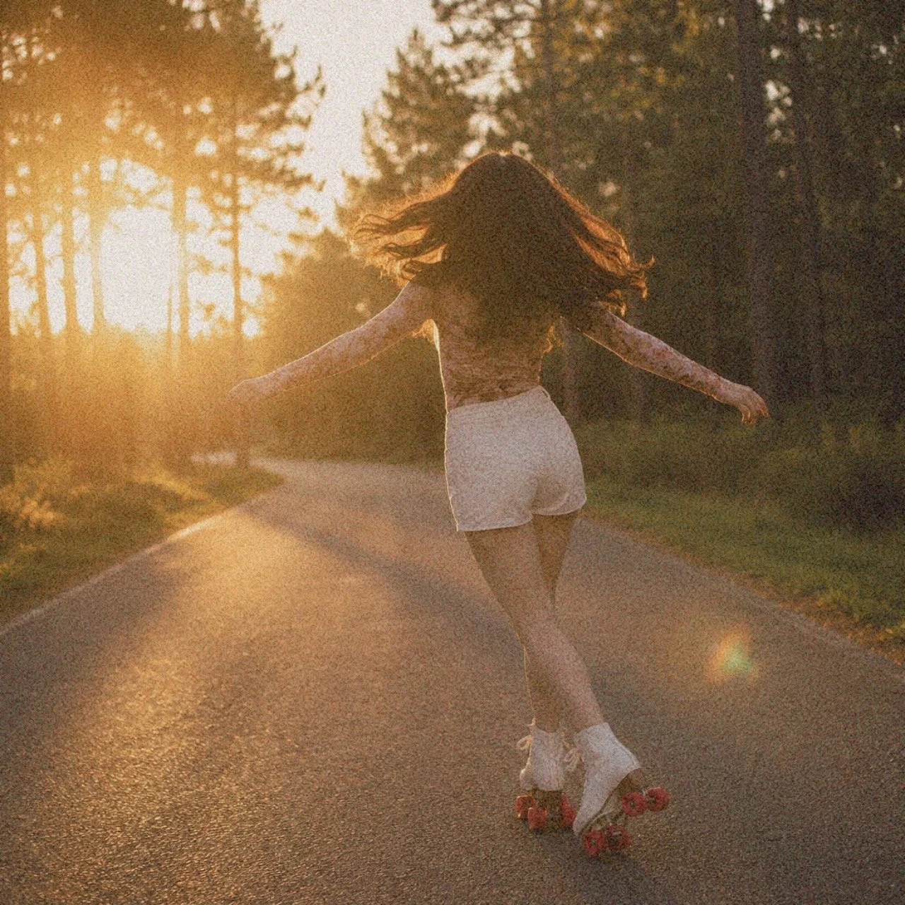 A woman roller-skating on a road during sunset, with her arms extended and hair flowing.