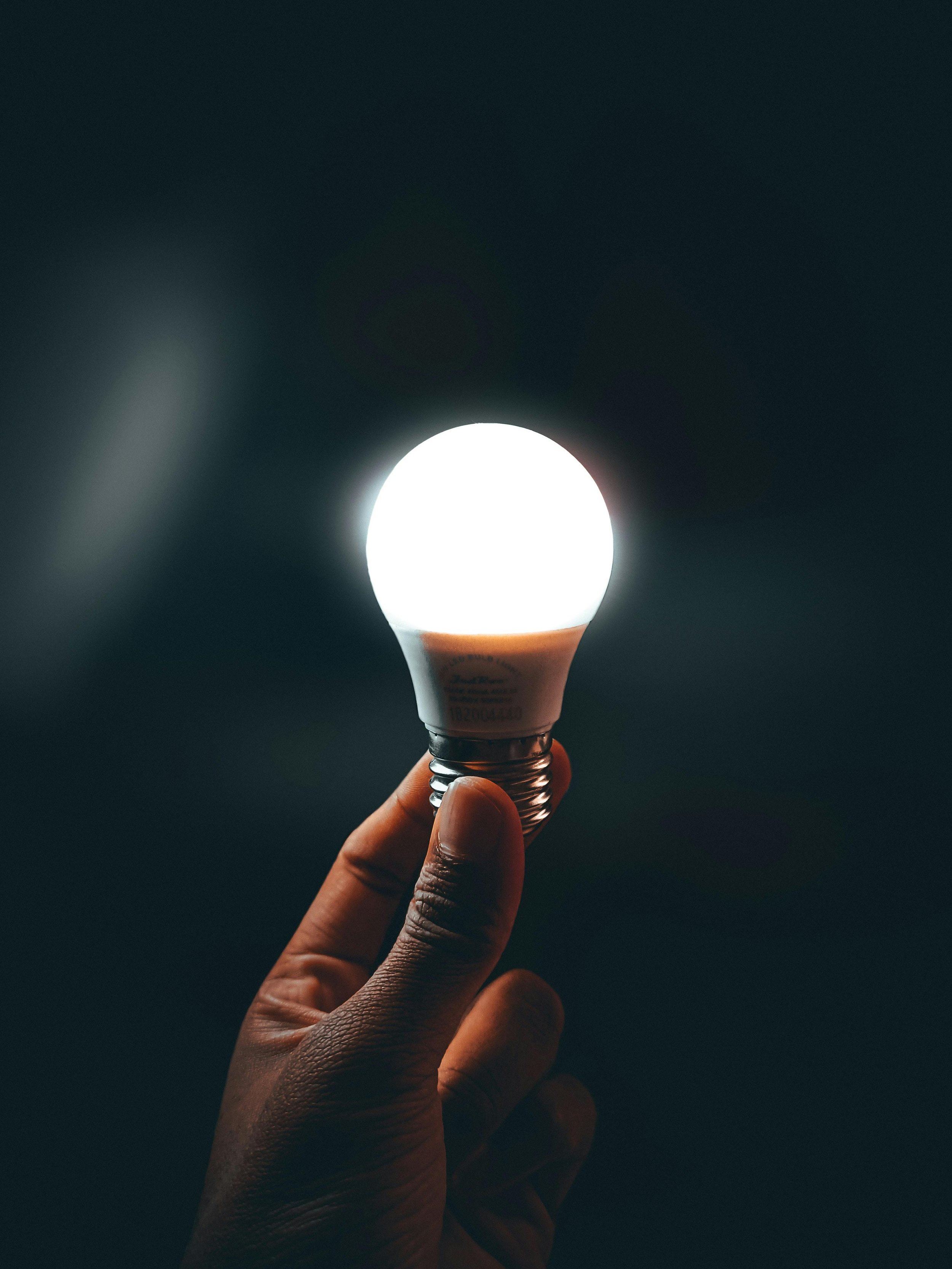 Una mano sostiene una lámpara LED con luz brillante en un fondo oscuro.