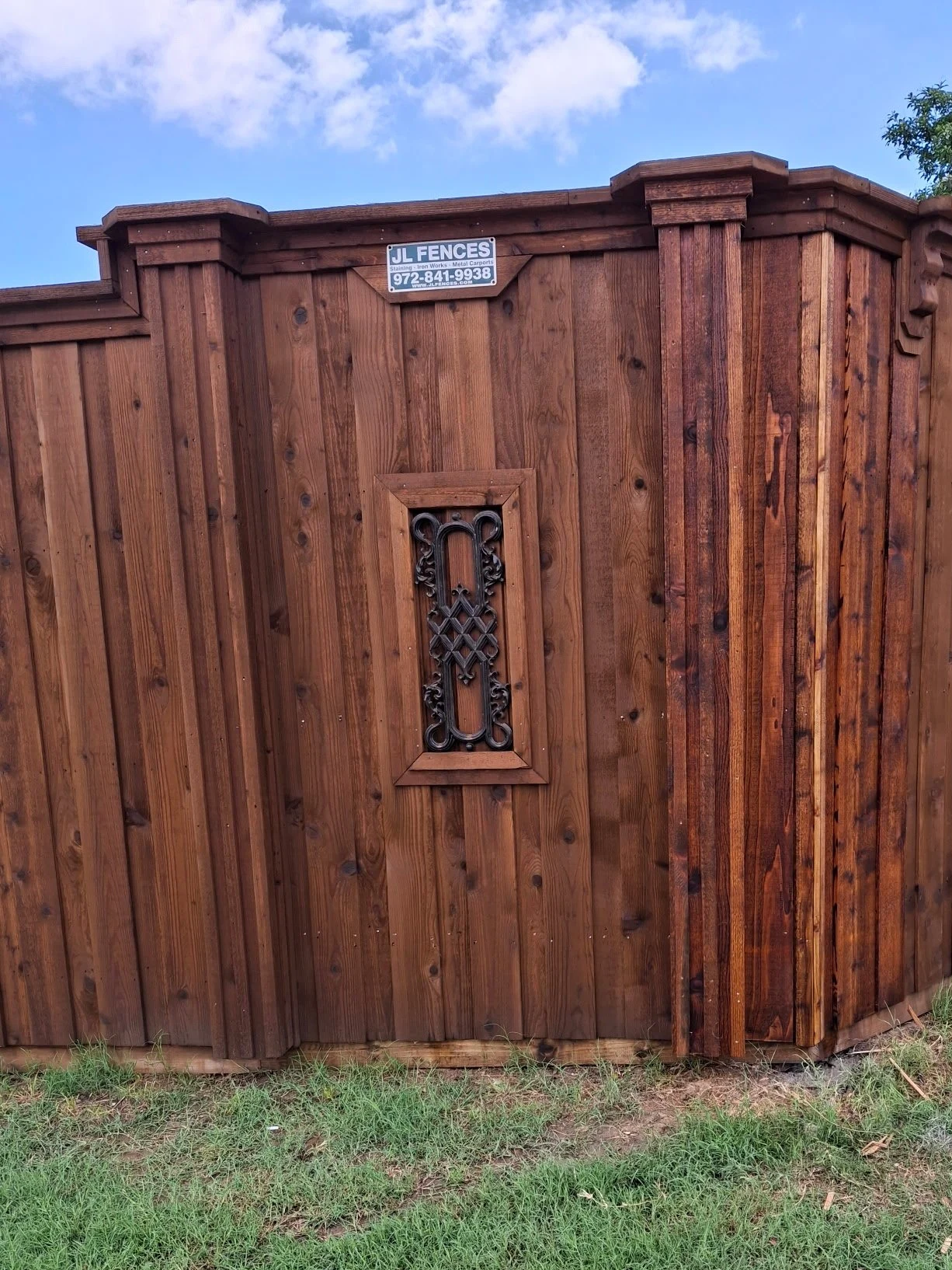 A large wooden fence with a decorative metal vent and a small informational sign at the top.