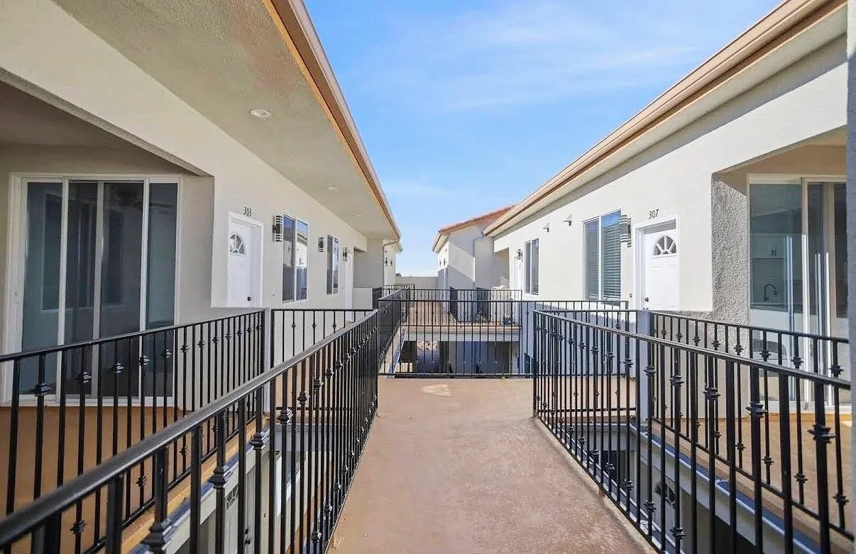 Balcony walkway between two apartment buildings with black metal railings and white doors labeled 303 and 307.
