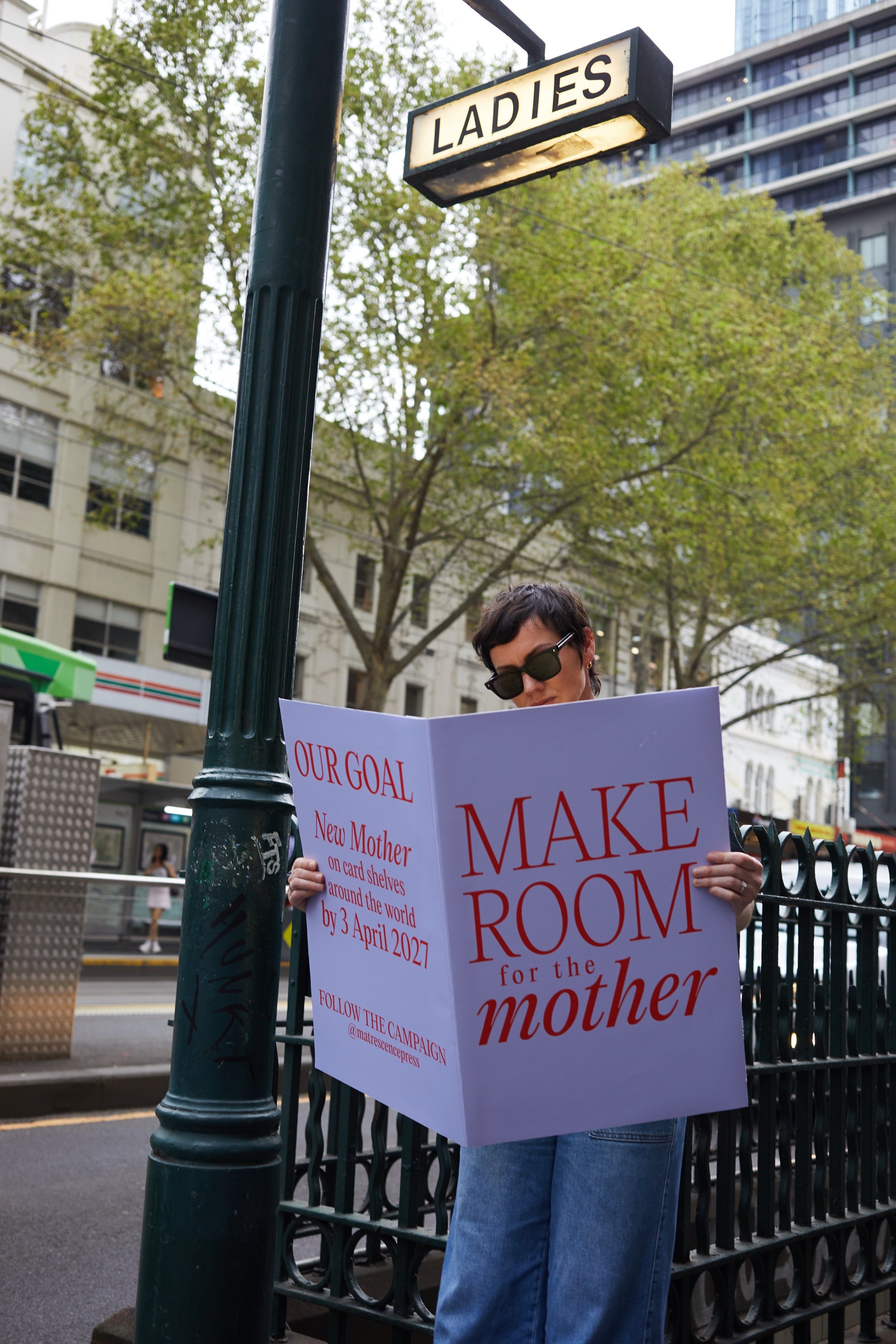 A woman holding a giant card that reads "MAKE ROOM for the mother", to promote the campaign