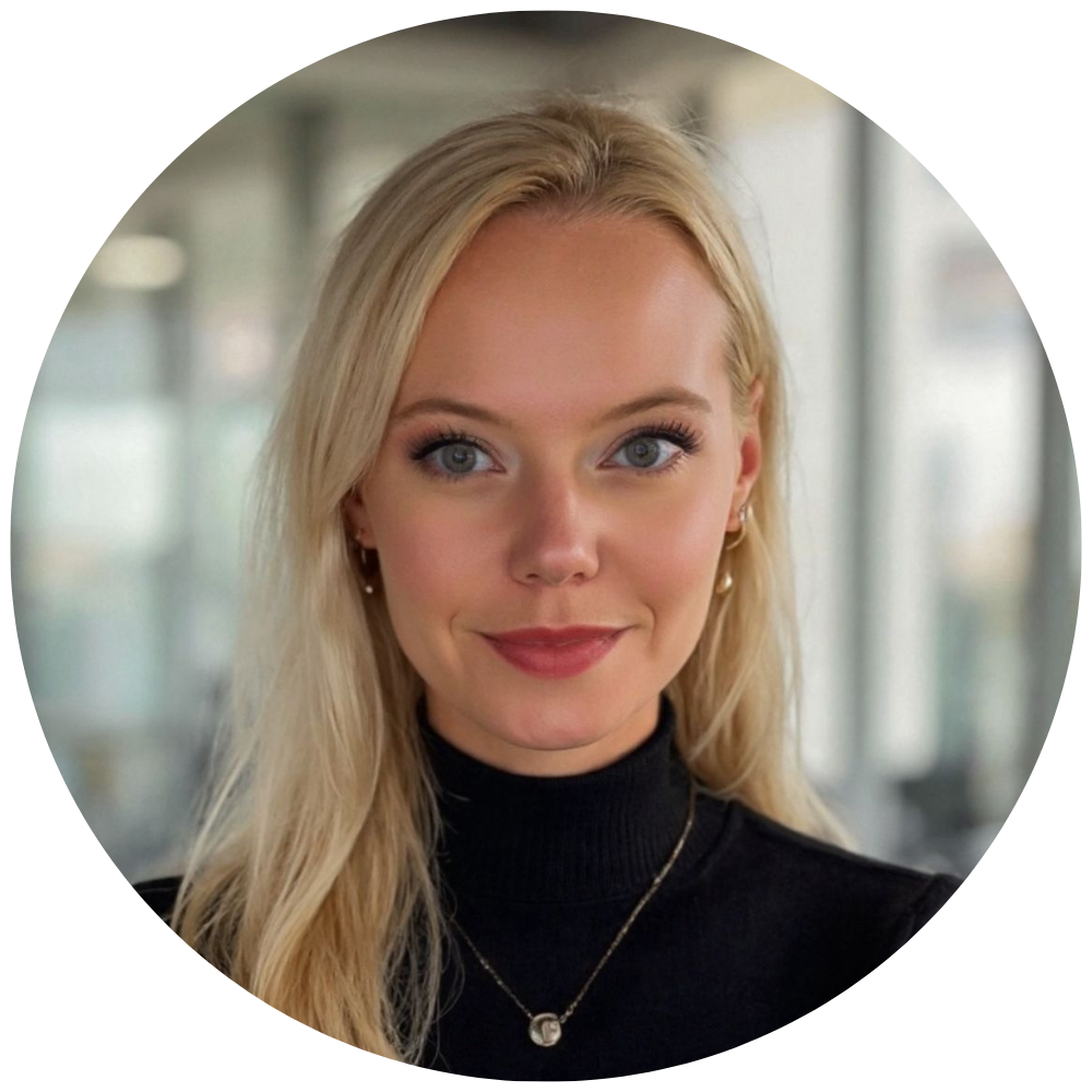 Coach Larissa, wearing a black turtleneck and a delicate necklace, indoors in a modern building with large windows.
