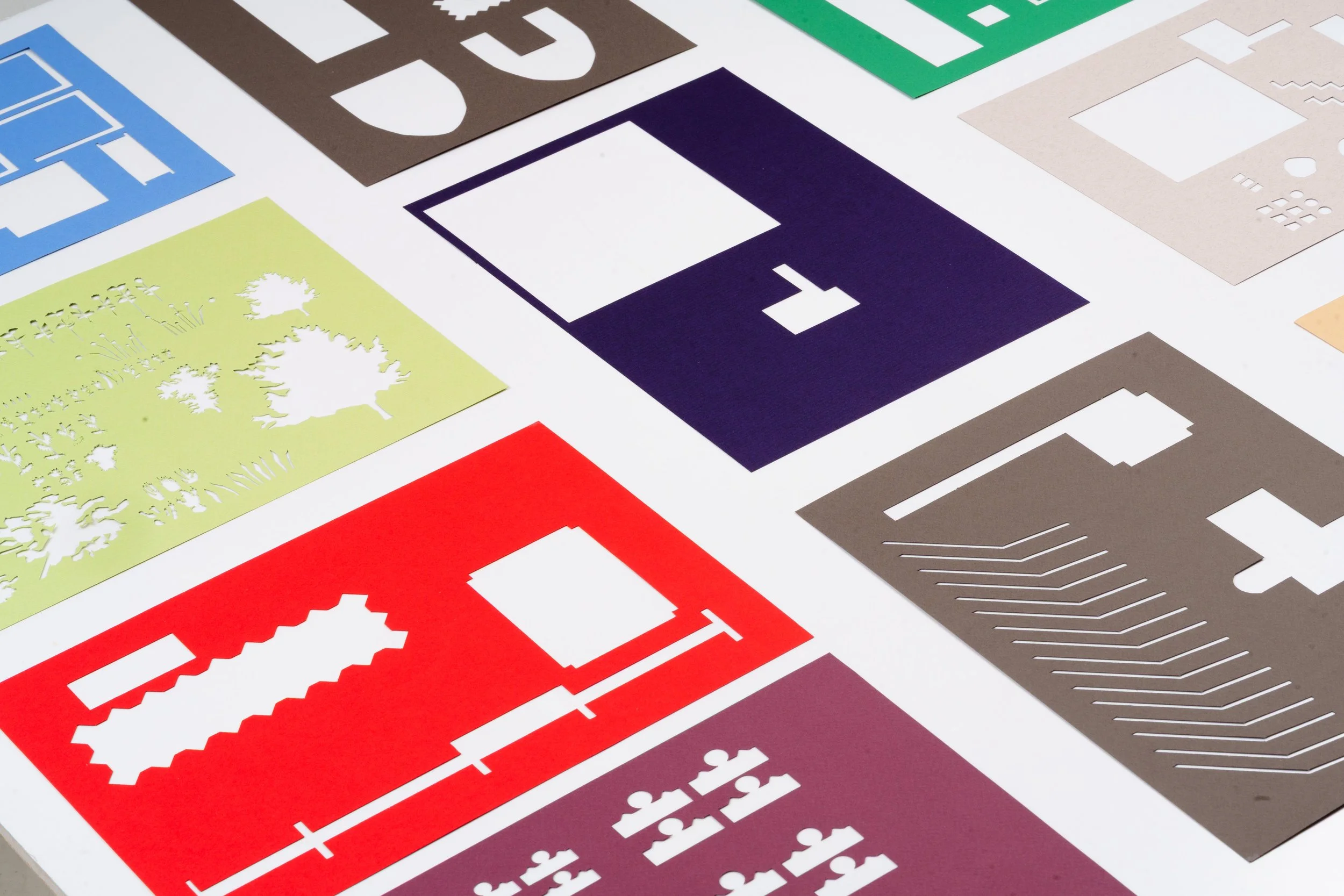 A collection of colorful paper cutouts featuring various shapes and designs, including trees, gears, and geometric patterns, arranged on a white background.