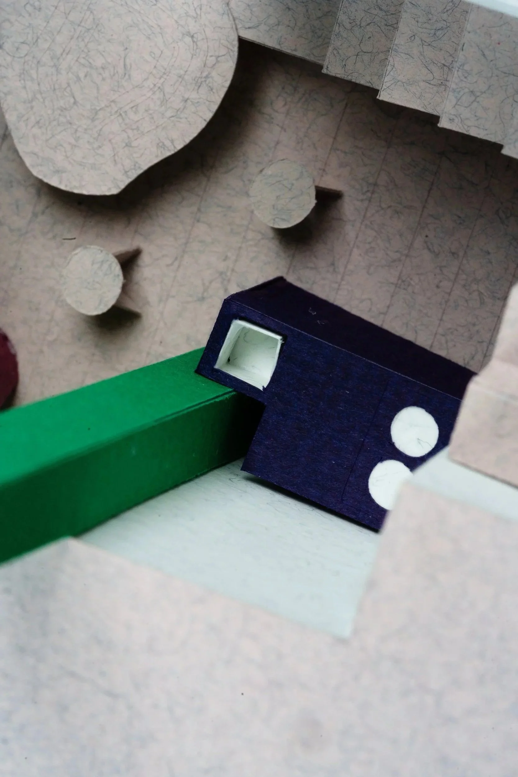 A close-up of a colorful, textured paper model with green, blue, and white sections and circular cutouts, crafted from construction paper or cardboard.