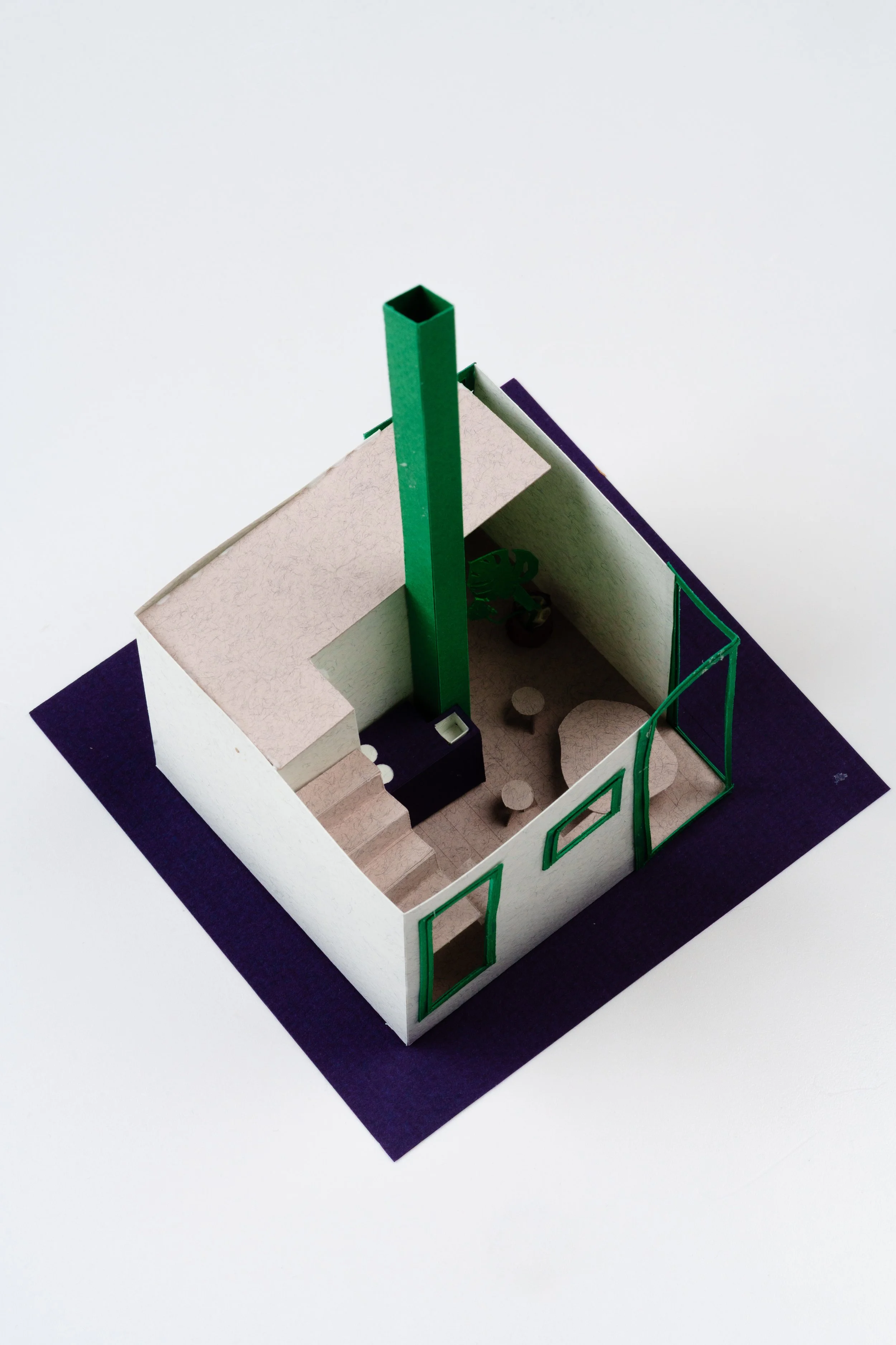 Minimalist architectural model of a small house with white walls, green accents, and a purple base, featuring a staircase, arched windows, and a potted plant inside.
